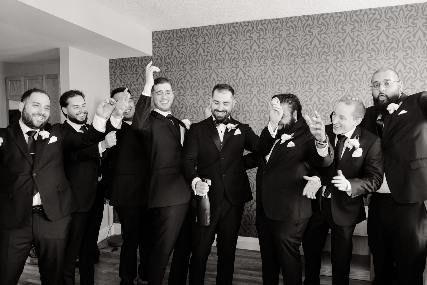 Black and white photo of groomsmen in formal attire posing together against a patterned wall.