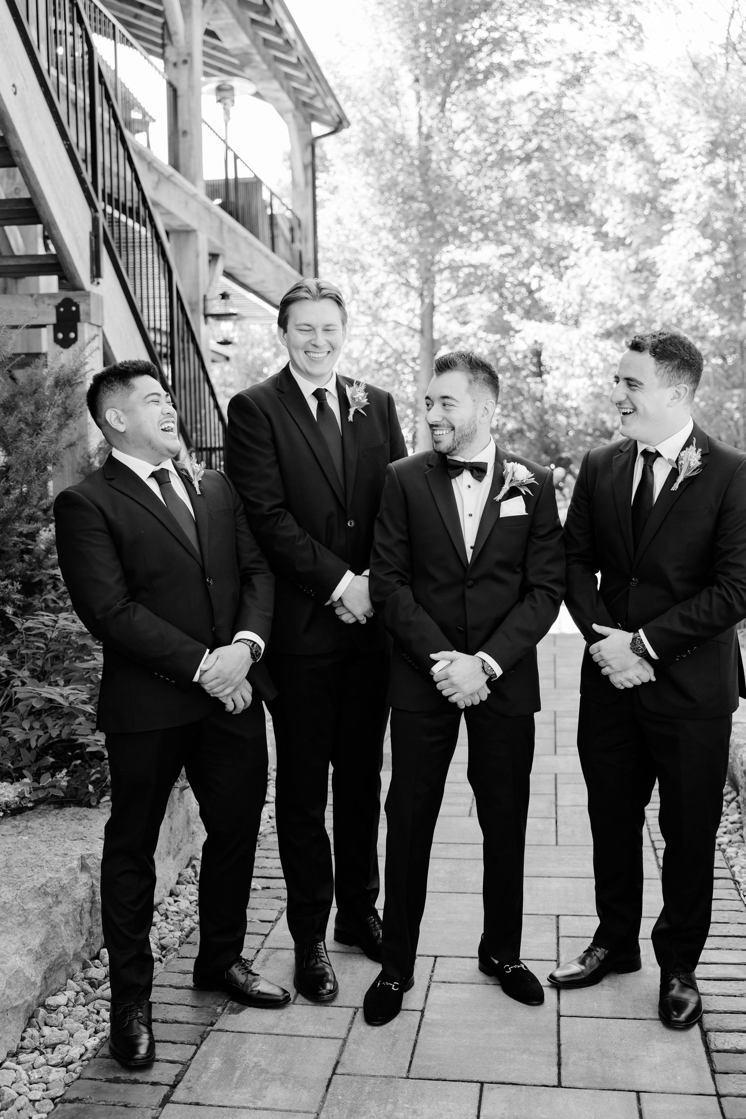 Black and white portrait of groomsmen laughing together on outdoor patio.
