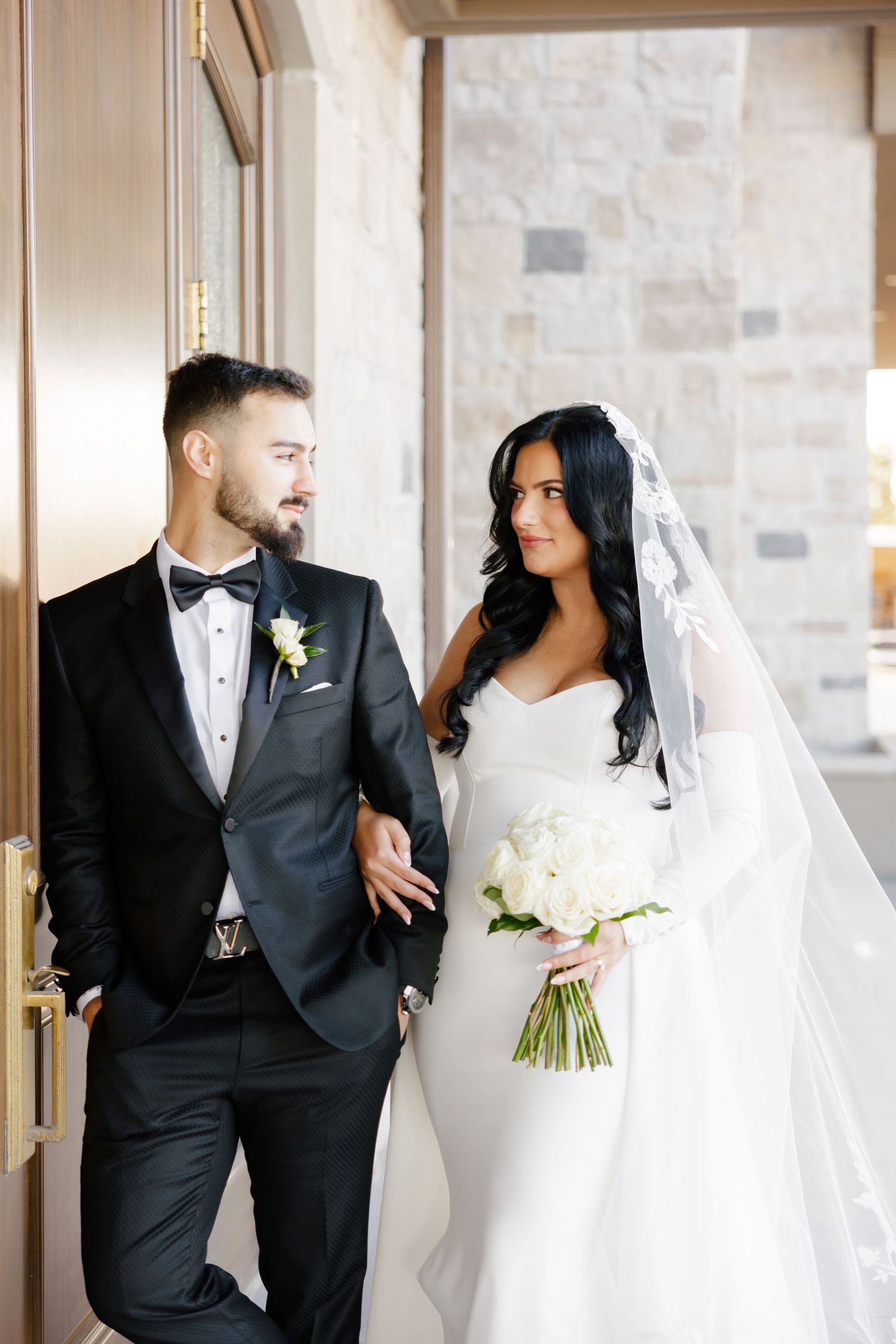 Stylish wedding couple shares intimate moment against stone wall backdrop.