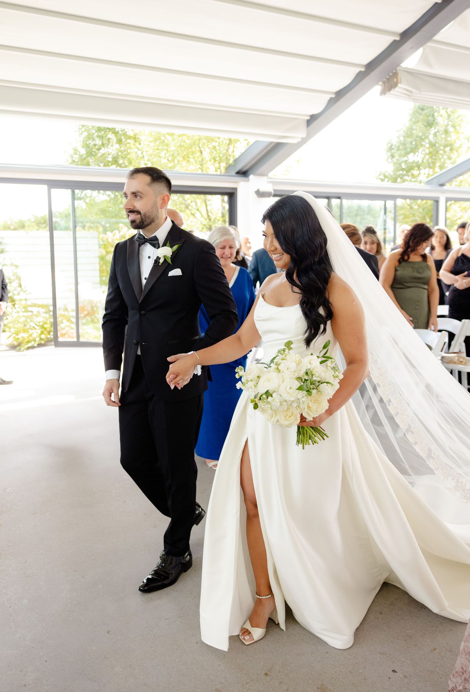 A couple walks together during their wedding ceremony in an elegant white venue.