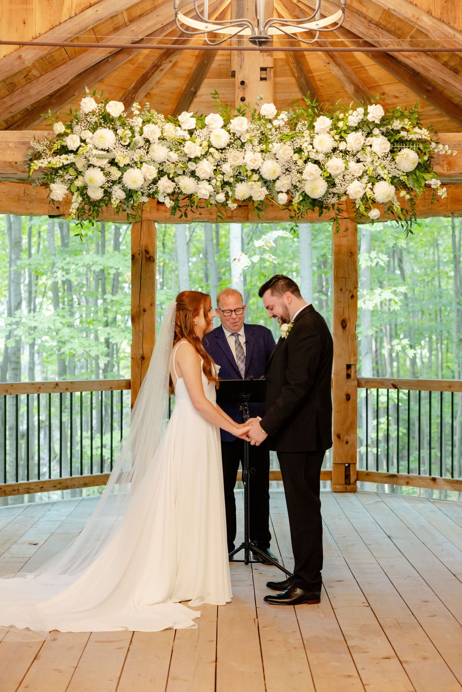 Wedding ceremony in a wooden gazebo with stunning floral chandelier and forest views.