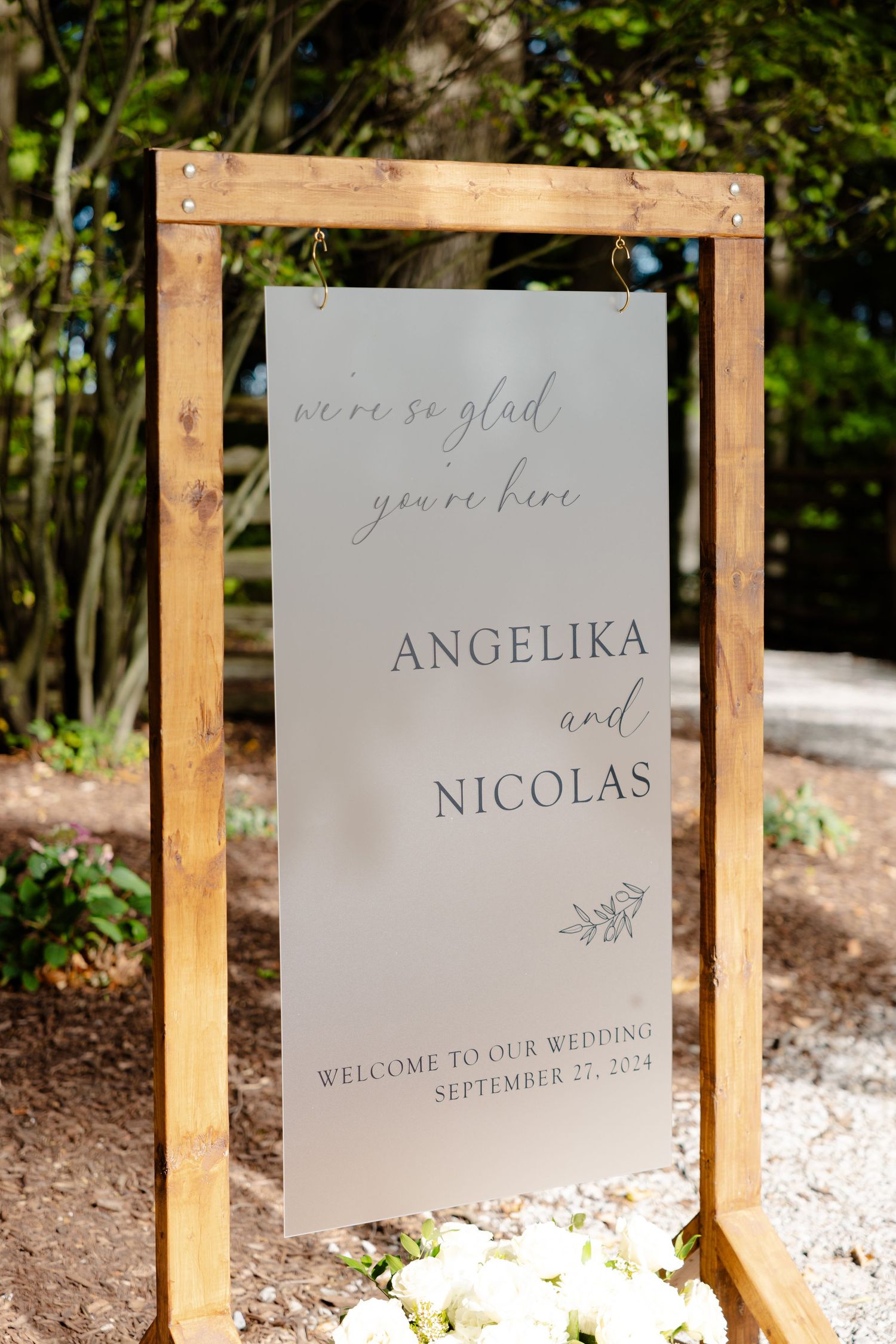 Wooden framed wedding welcome sign with minimalist gray design displayed in garden setting.