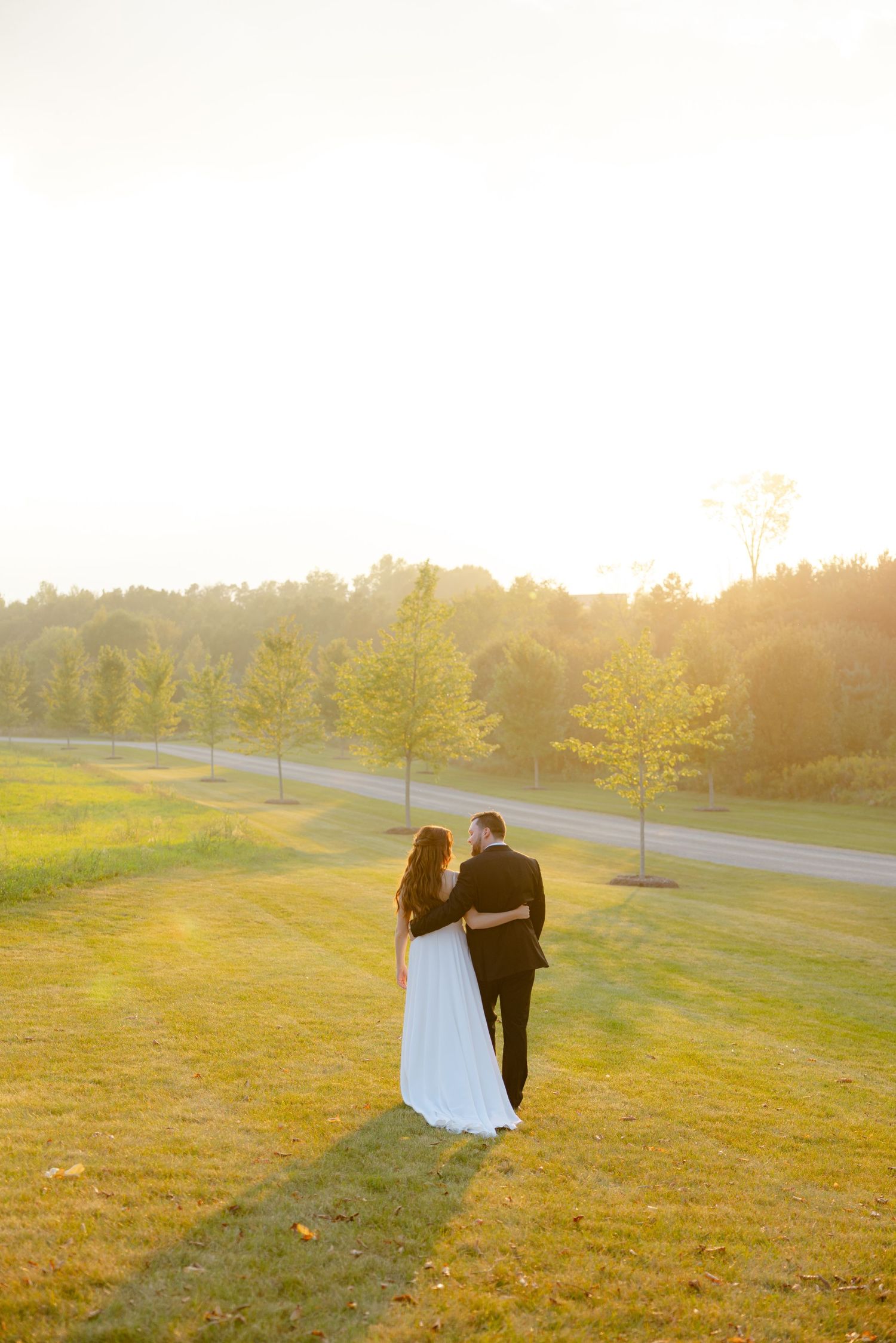 A wedding couple walks together on a scenic hilltop during golden hour surrounded by autumn trees.