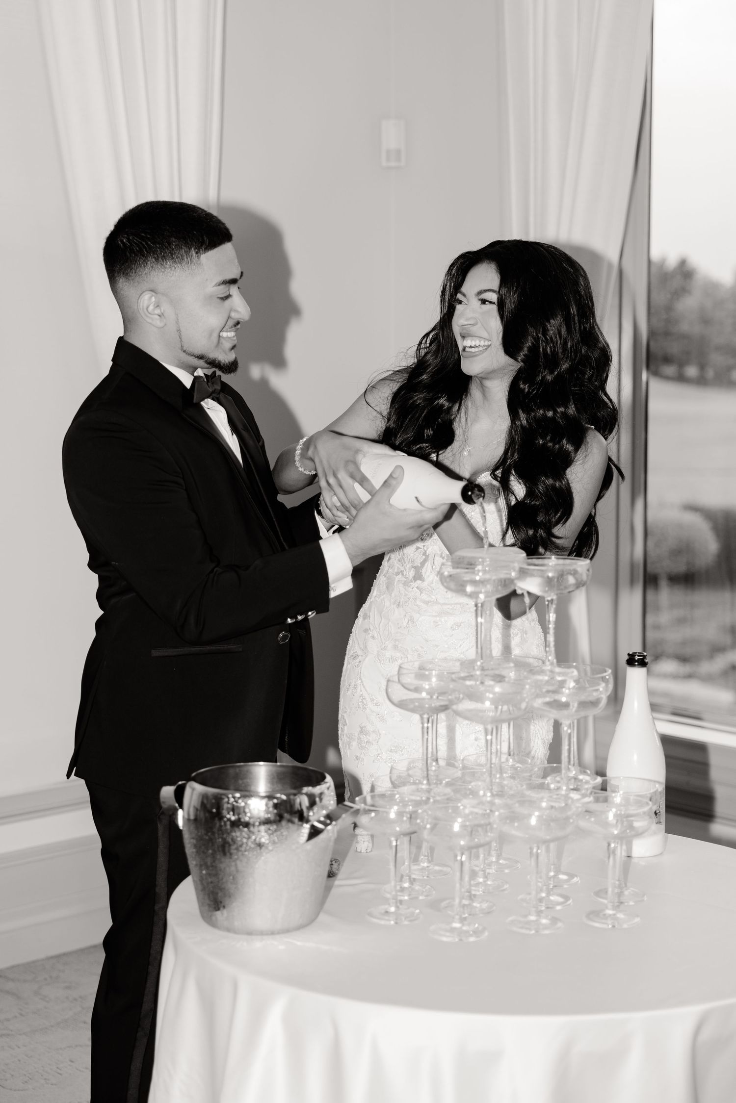 Black and white photo of a couple pouring champagne together at their wedding celebration.