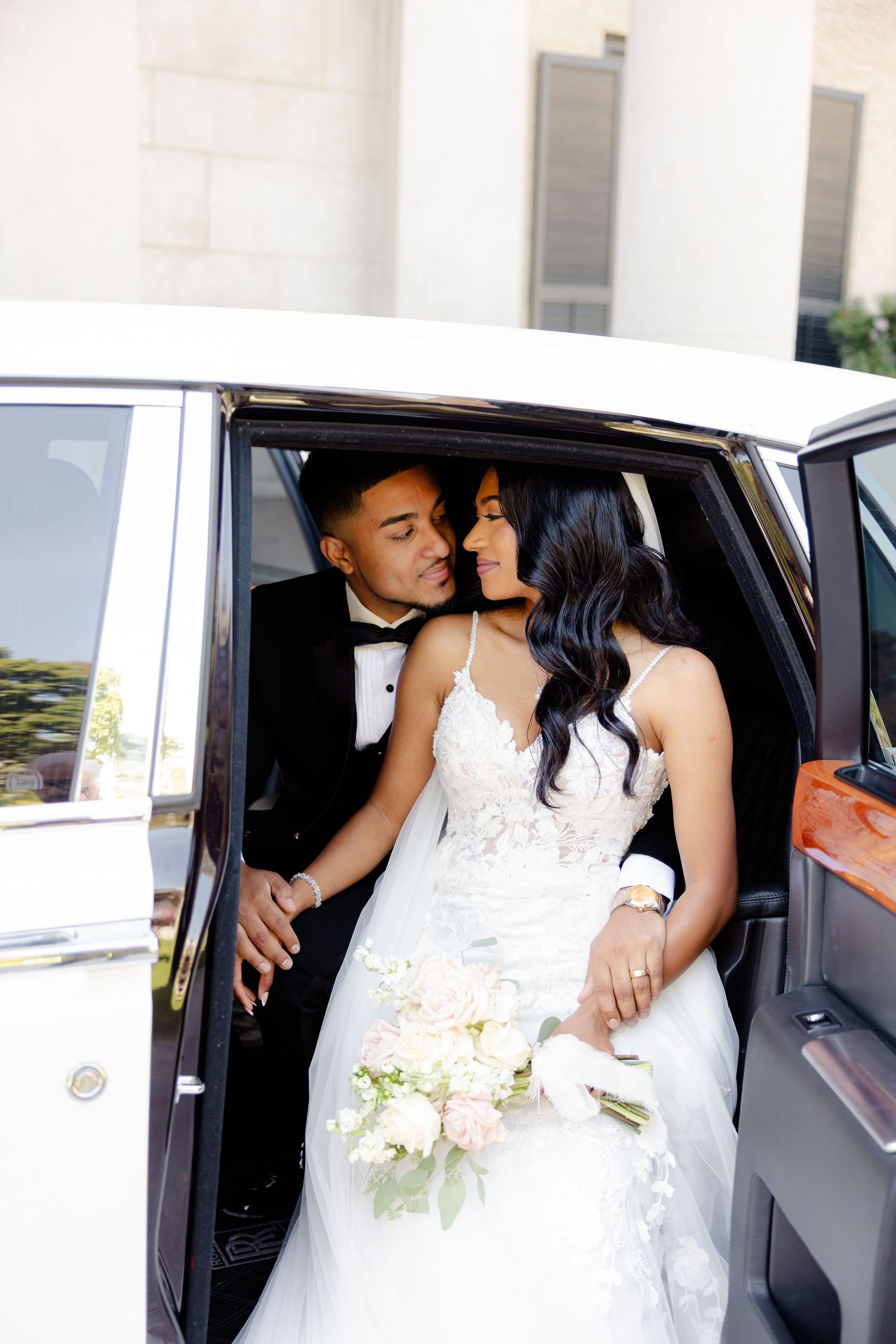 Intimate moment between newlyweds inside a luxury white car with bouquet.
