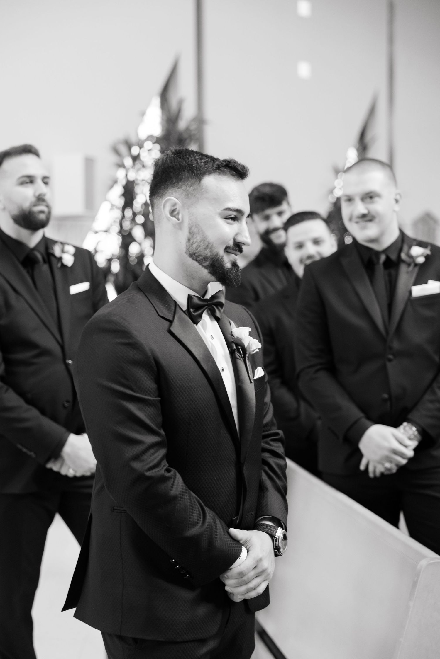 A black-tie wedding party in formal attire shares a moment at the altar.