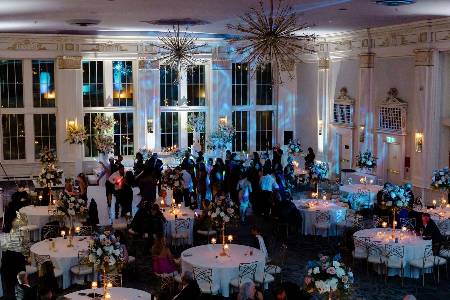 Panoramic view of dimly lit wedding reception hall with elegant table settings and chandeliers.