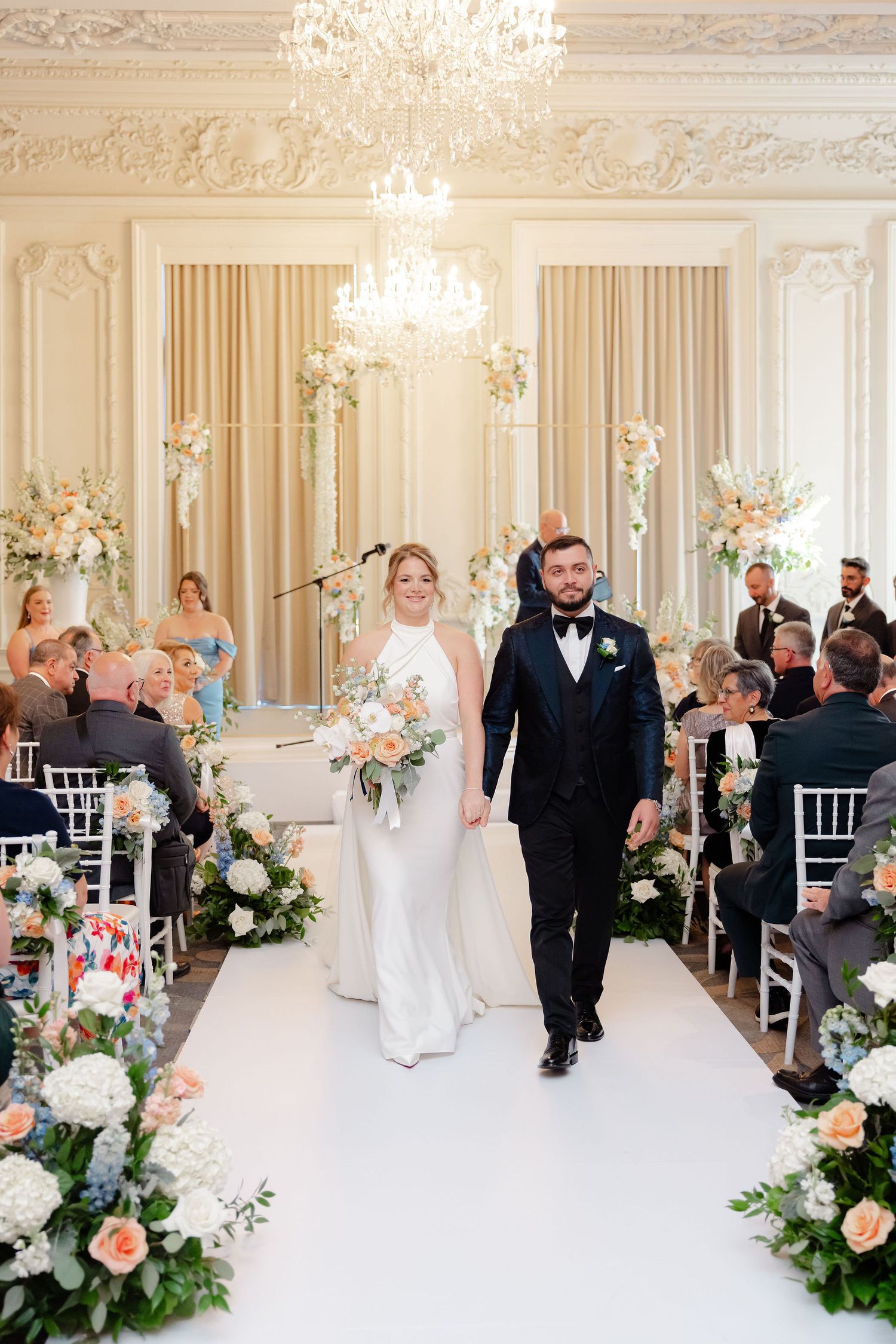 Elegant wedding ceremony space with floral arrangements, white chairs, and crystal chandeliers.