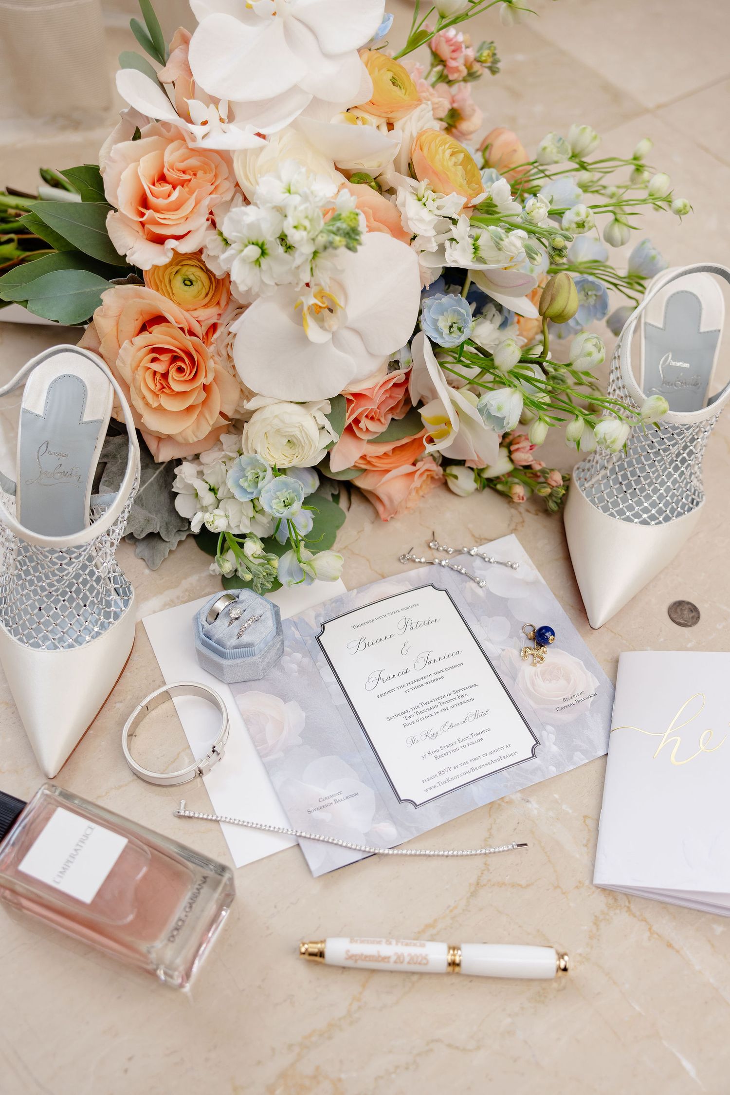 Elegant wedding flatlay with peach and white flowers, stationery, and silver high heels on marble surface.