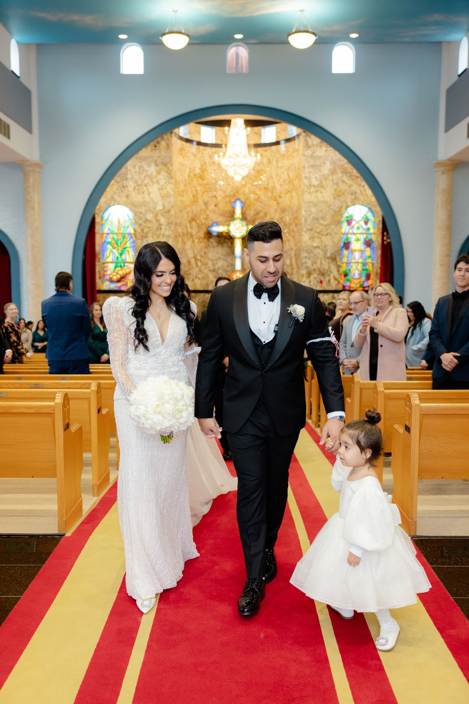 Wedding recessional down ornate church aisle with flower girl in white dress.