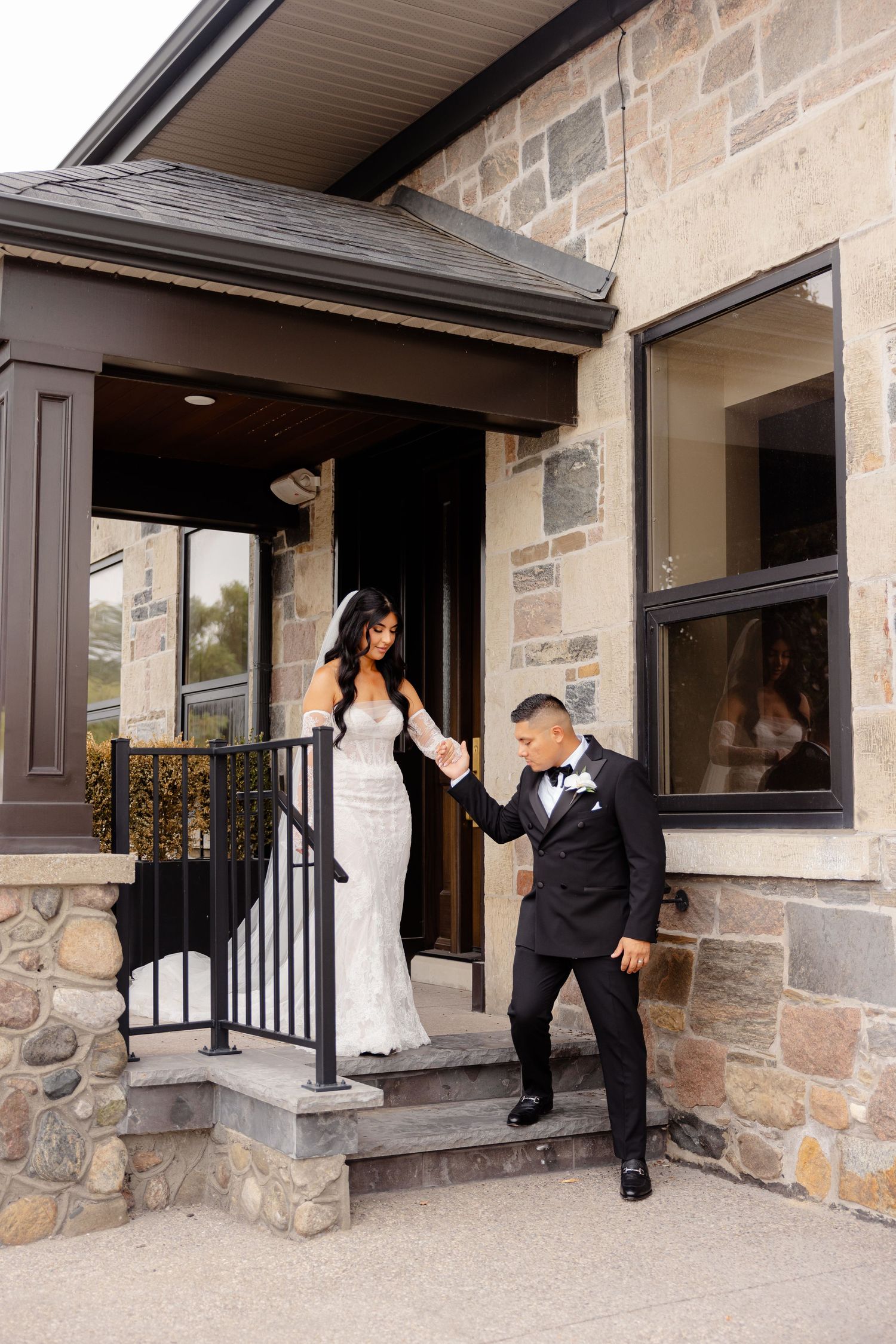 People in formal attire posing playfully at different angles around a building entrance with stone and brick walls.