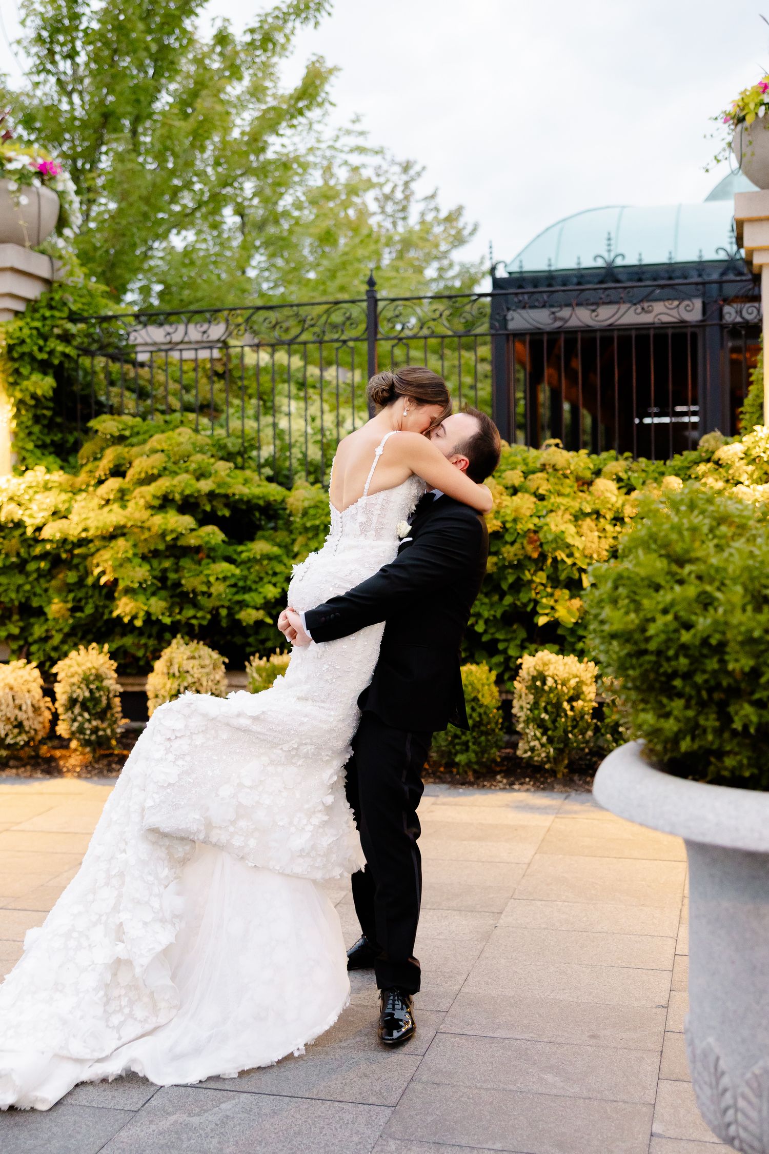 A couple in wedding attire dances and dips romantically on an outdoor terrace surrounded by autumn foliage.