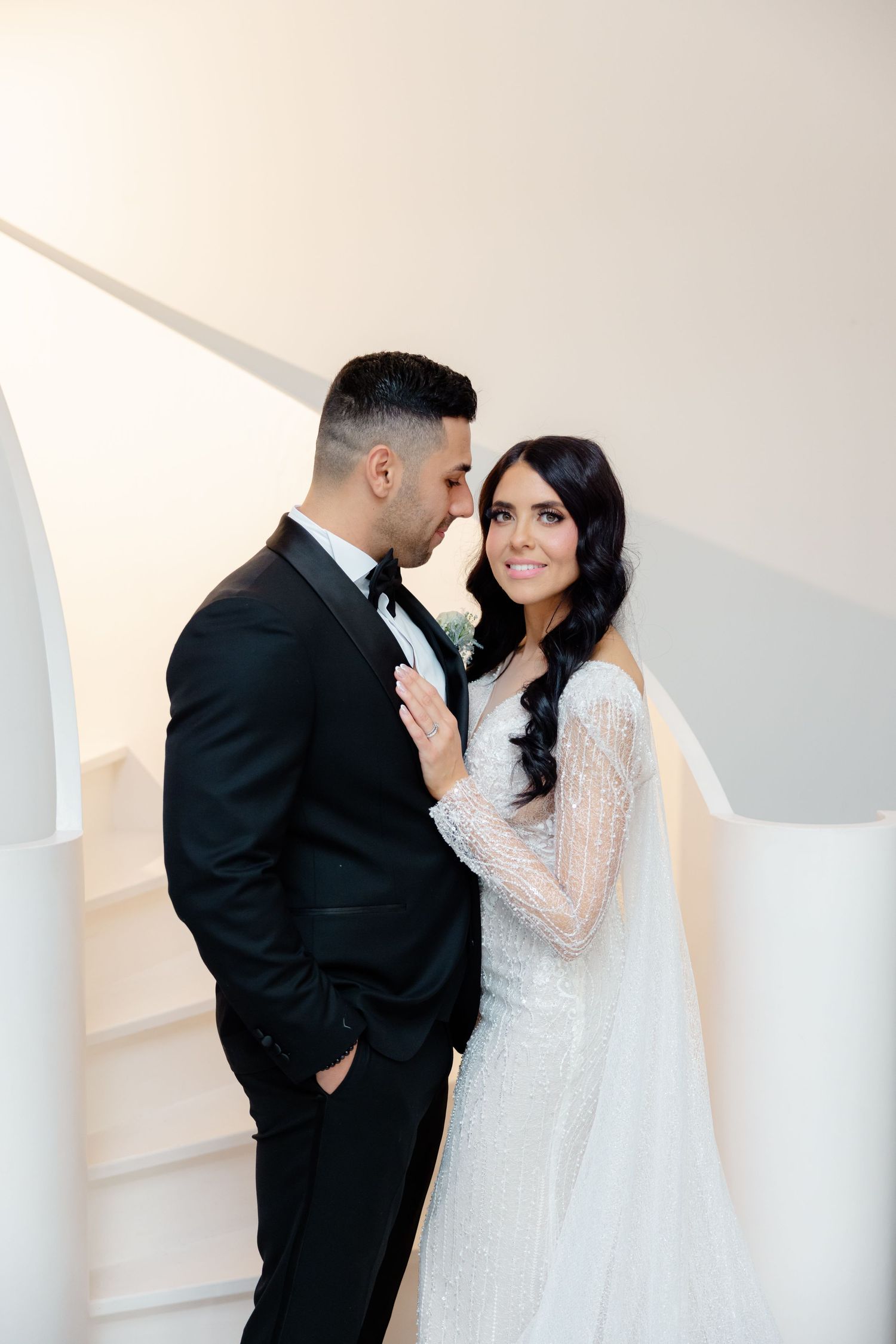 Romantic wedding photo of couple sharing tender moment against white modern backdrop.