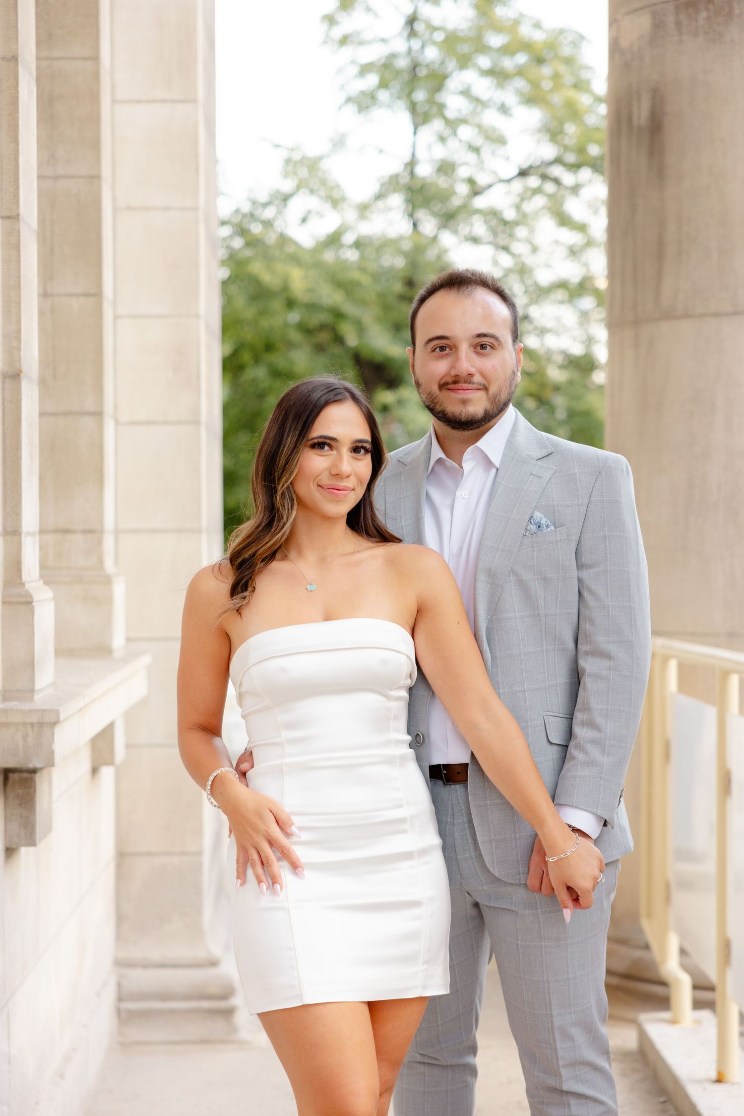 Couple dressed in white and gray pose together in an elegant colonnade setting.