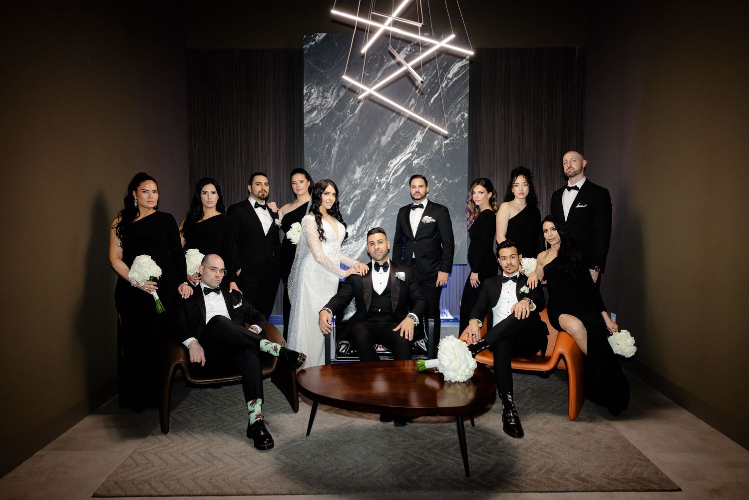 Formal wedding party gathered around circular table in modern venue with geometric lighting.