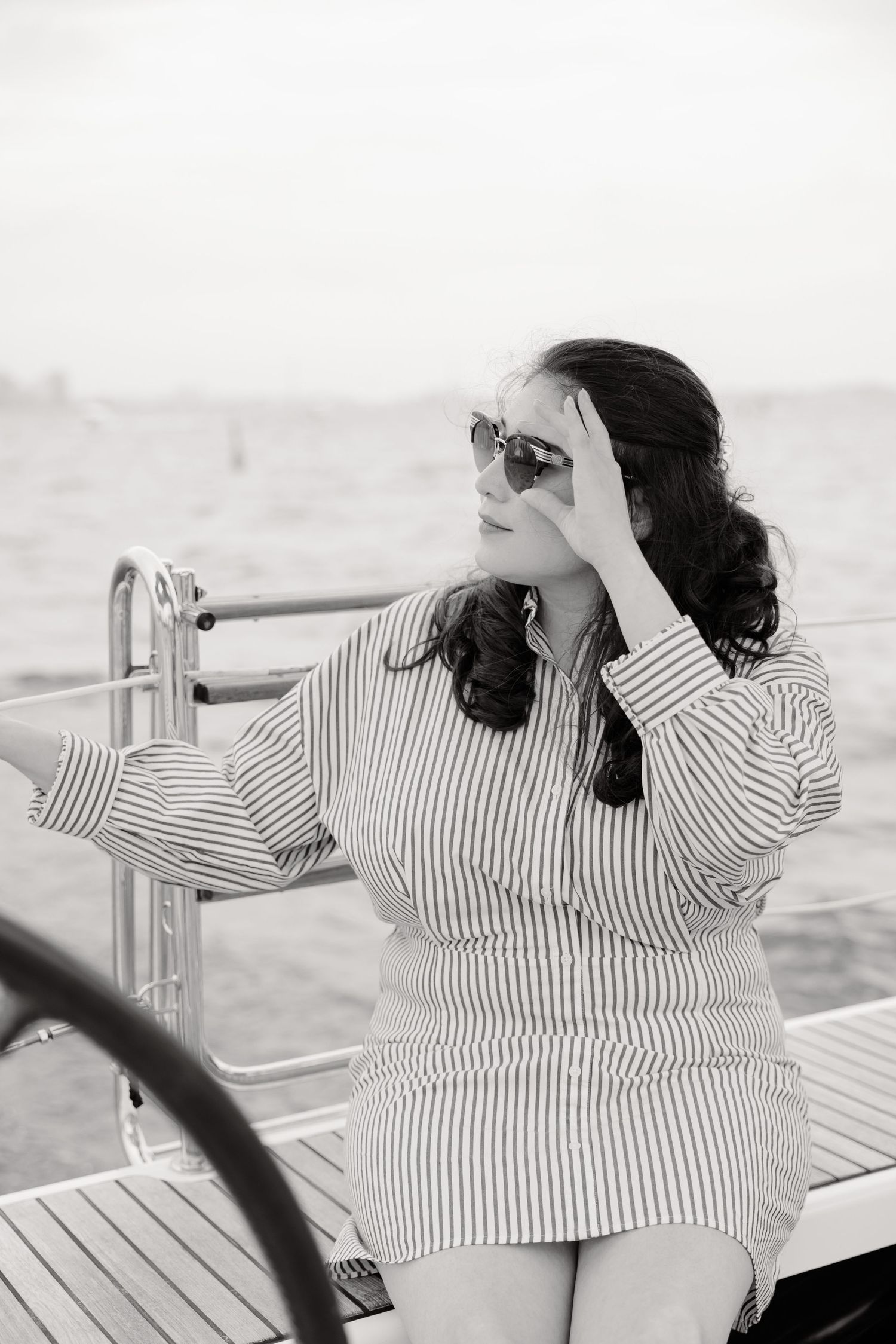A person in striped shirt and sunglasses relaxing on a boat deck in black and white photography.