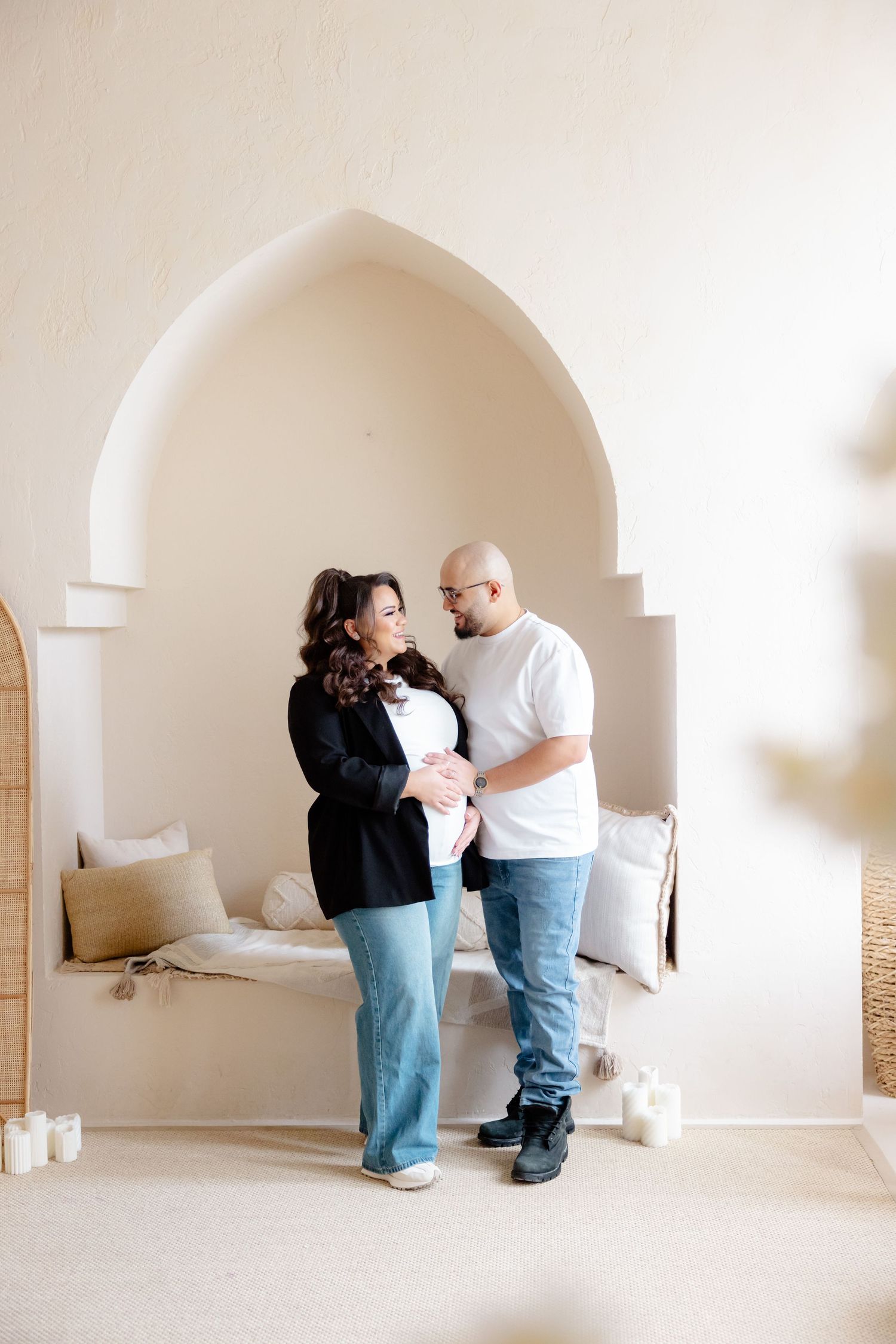A couple stands together in front of an arched alcove with neutral decor and soft lighting.