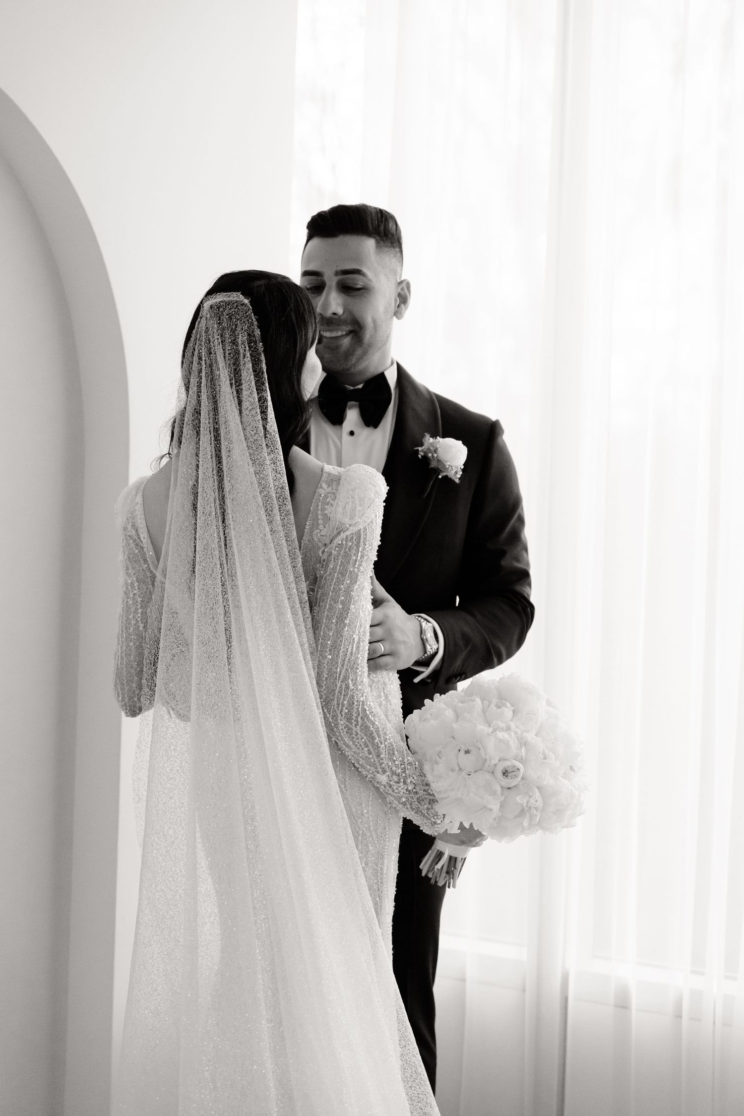 Black and white wedding portrait of couple sharing intimate moment under archway.