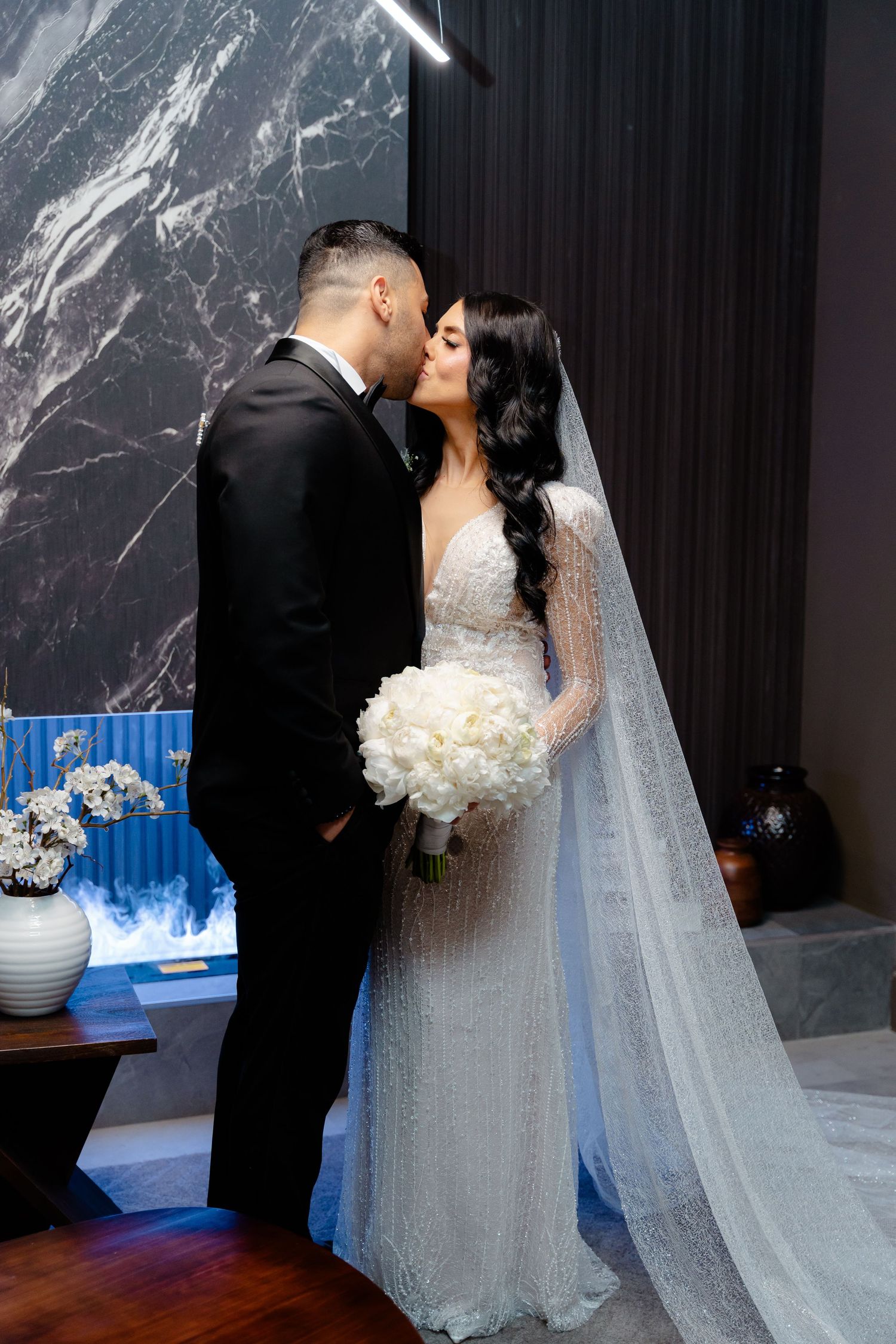 Wedding couple shares a kiss in an elegant venue with marble walls and blue accents.