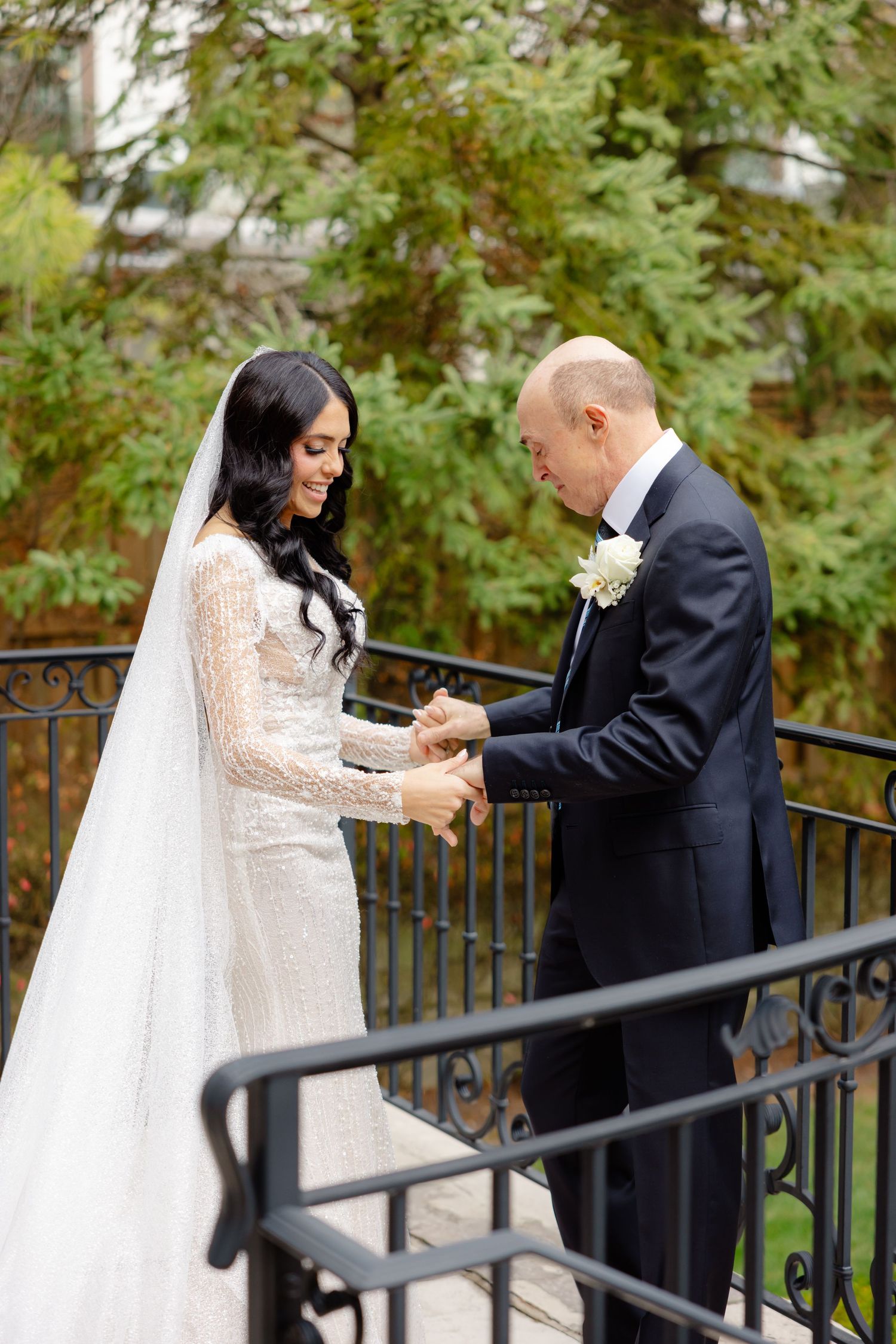 A tender moment between newlyweds as they hold hands on a stone terrace surrounded by fall foliage.