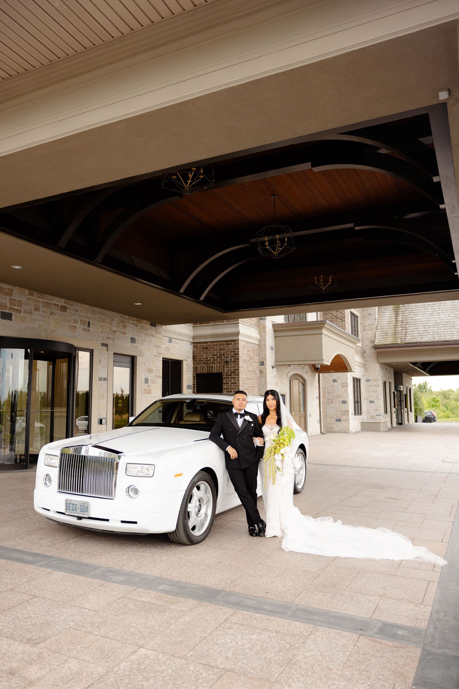 Luxury white Rolls Royce wedding car parked under covered driveway entrance of brick building.