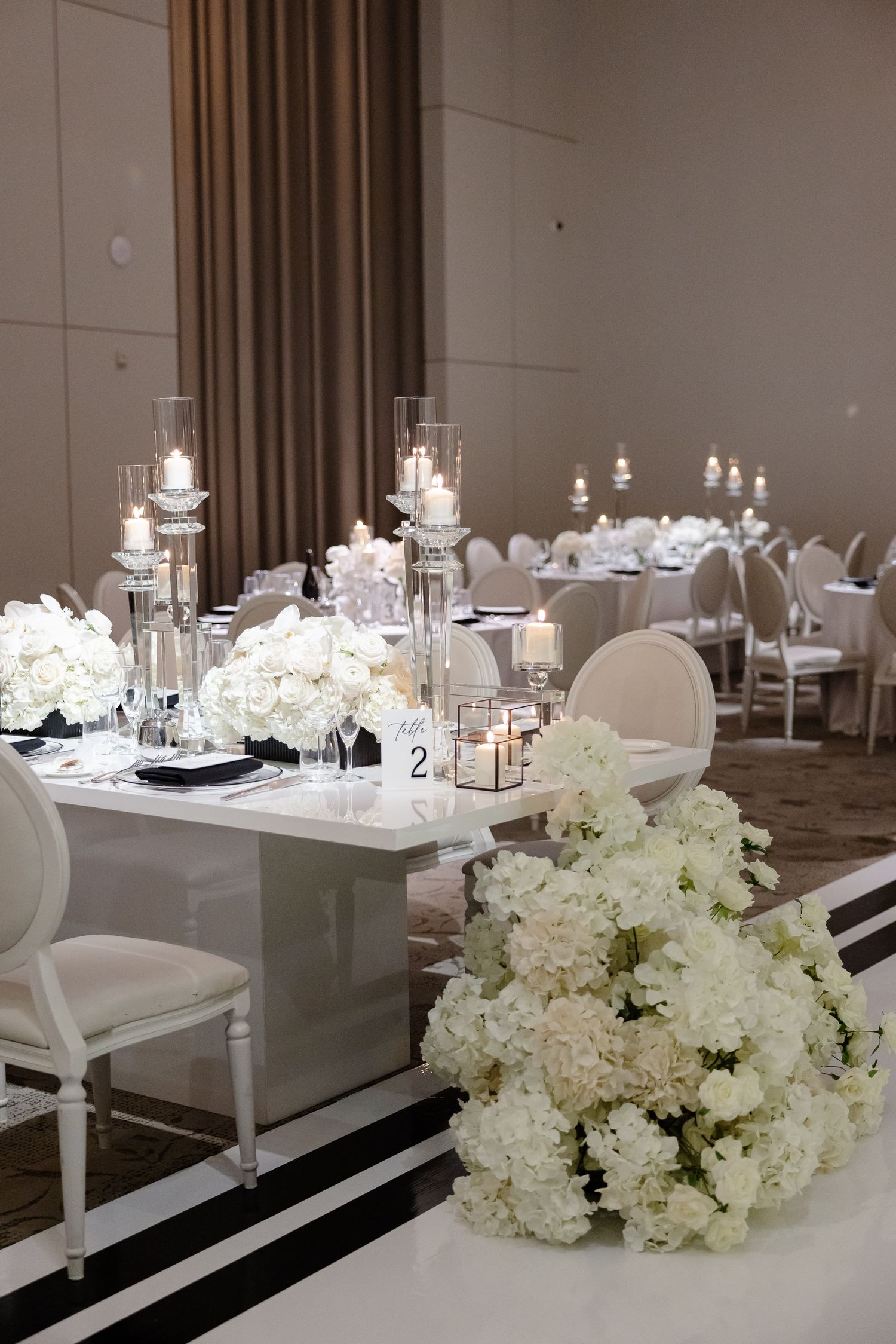 Modern white and grey wedding reception tables feature elegant floral centerpieces and crystal glass accents.