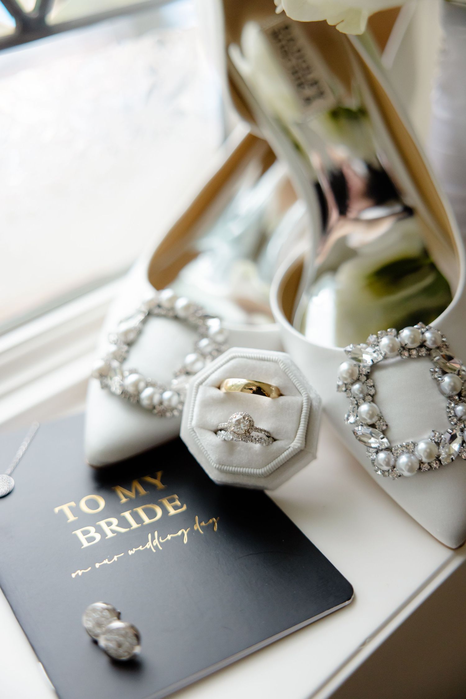 Wedding accessories including white heels, rings, and card displayed on windowsill.