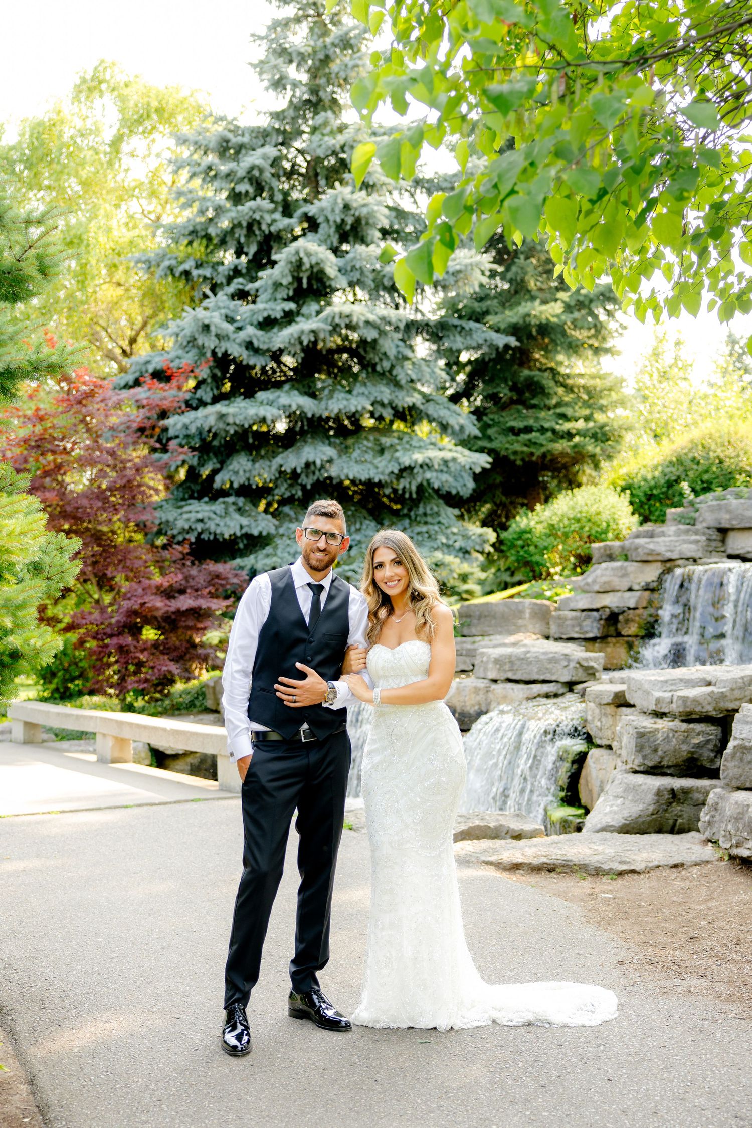 Elegant wedding portrait with stone waterfall and evergreen trees as backdrop.