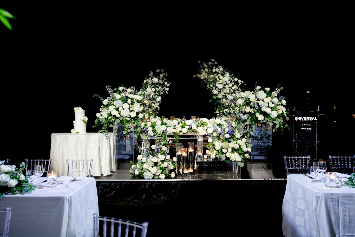 Wedding reception setup with dramatic white floral arrangements and chiavari chairs.
