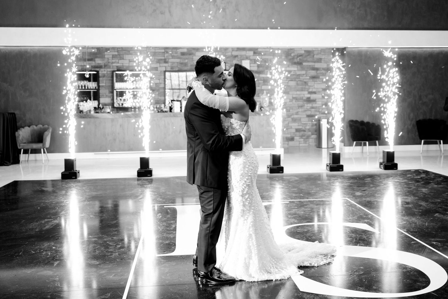 Black and white photo of a romantic first dance moment at an elegantly lit indoor venue.
