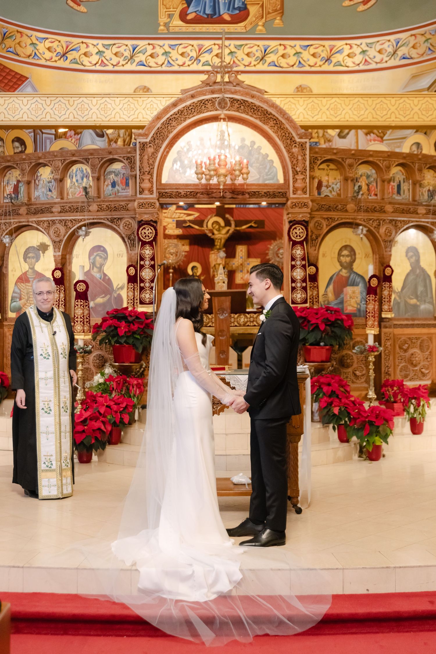 Traditional Orthodox wedding ceremony with priest officiating before ornate gold iconostasis.
