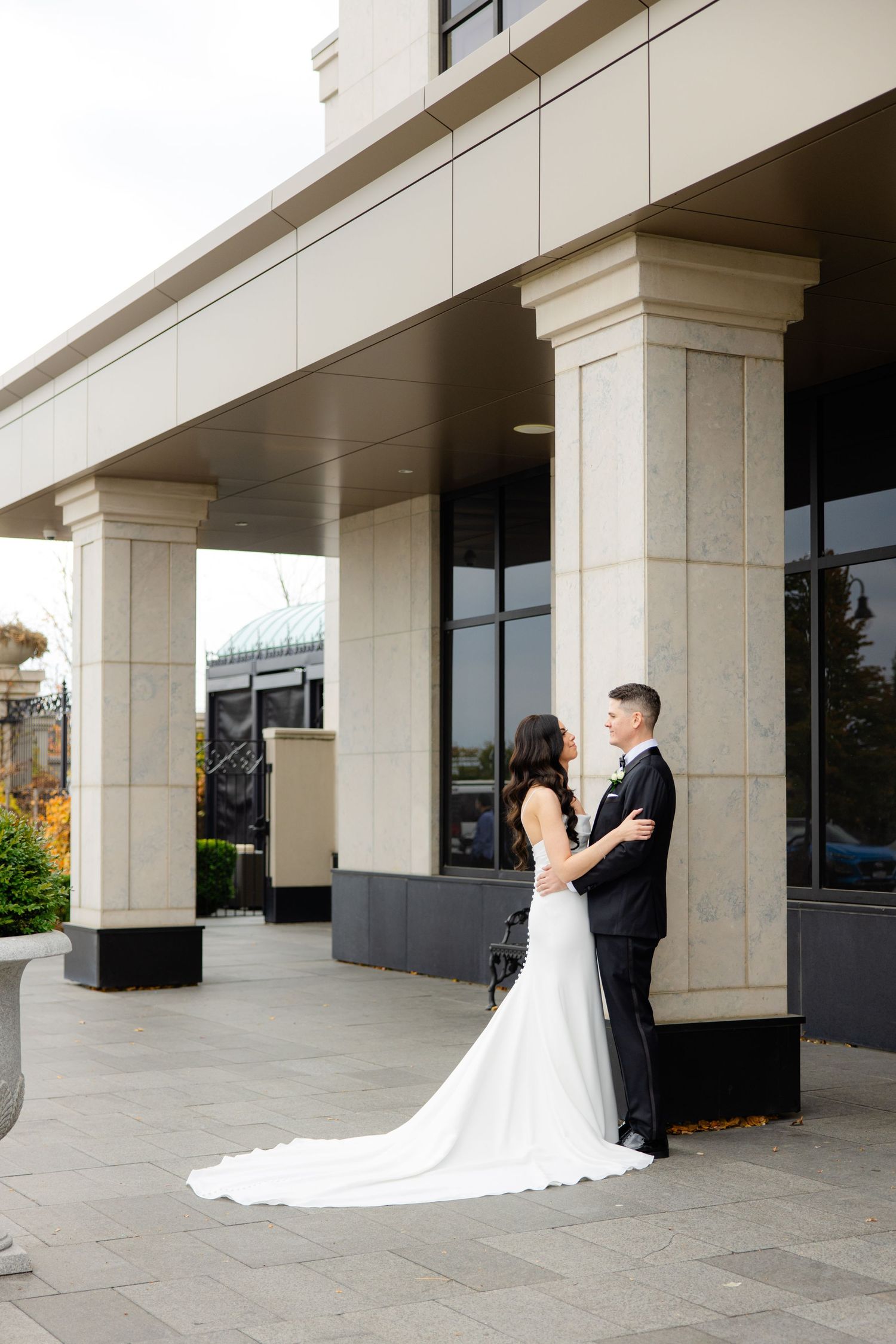 Wedding couple poses elegantly against modern architecture with columns and glass windows.