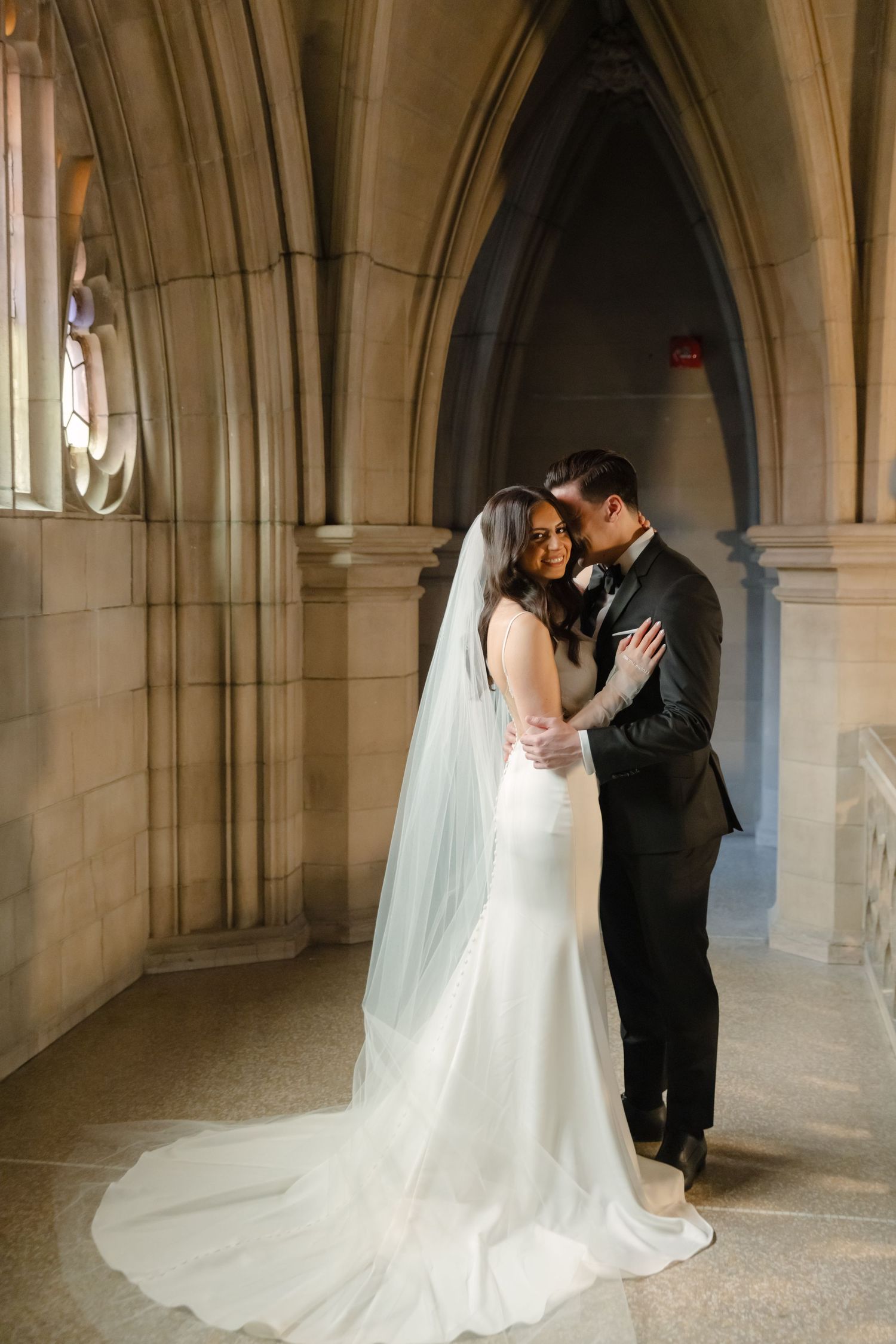 A romantic wedding moment captured in a gothic stone archway as newlyweds share an intimate embrace.