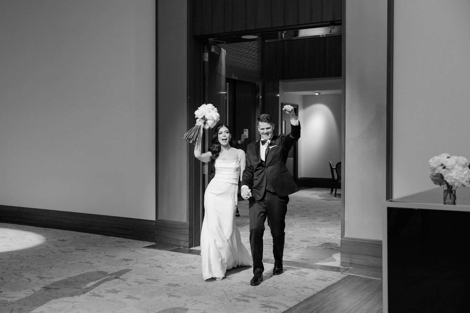 A black and white photo of a couple making their grand entrance through doorway at a wedding reception.