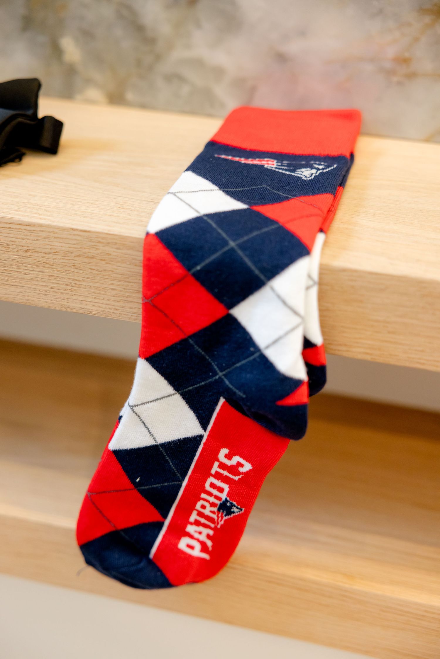 Red, white and navy argyle Patriots team sock displayed on wooden shelf.