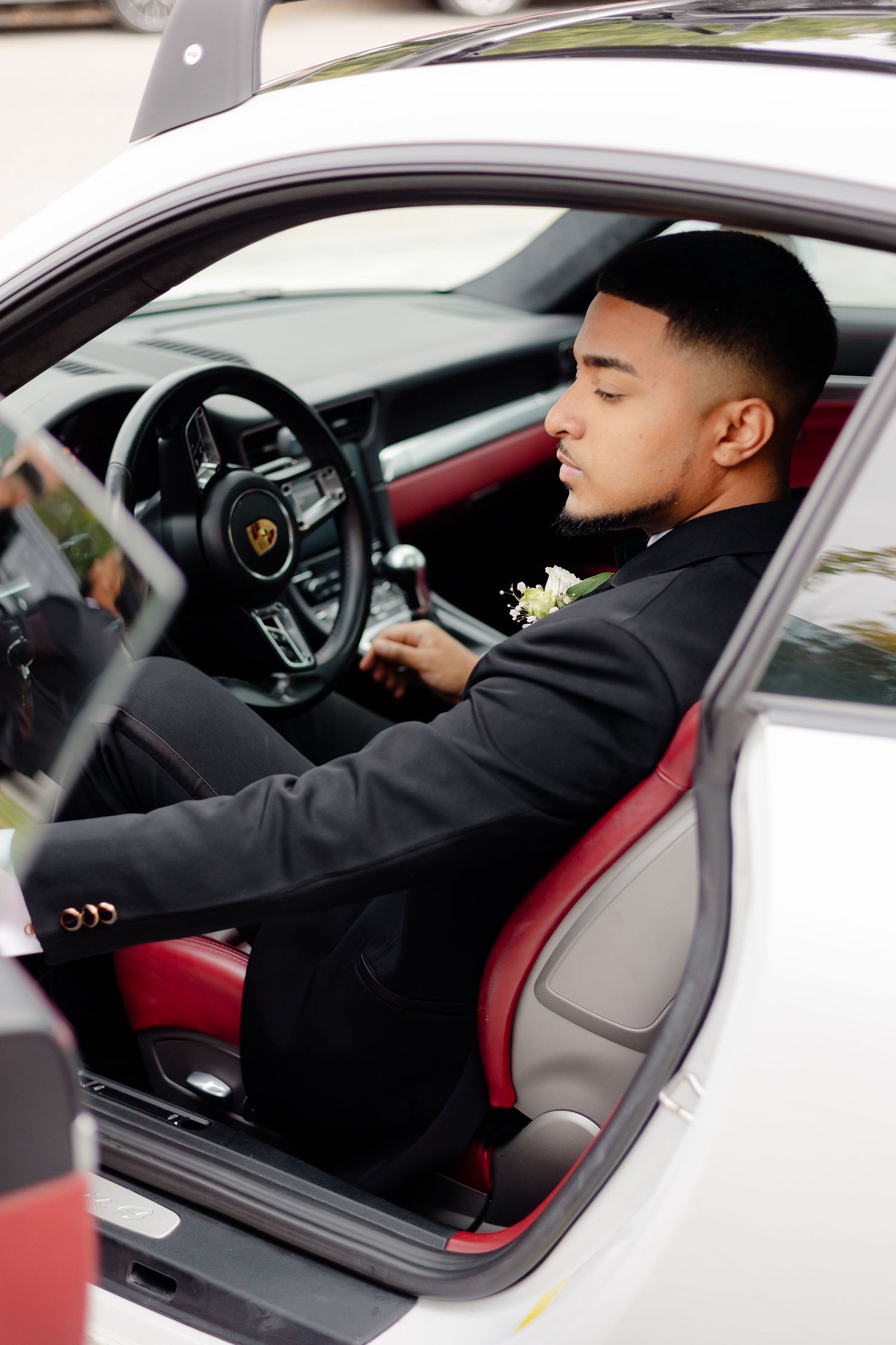 Wedding guest in black suit sitting in luxury car with red interior.