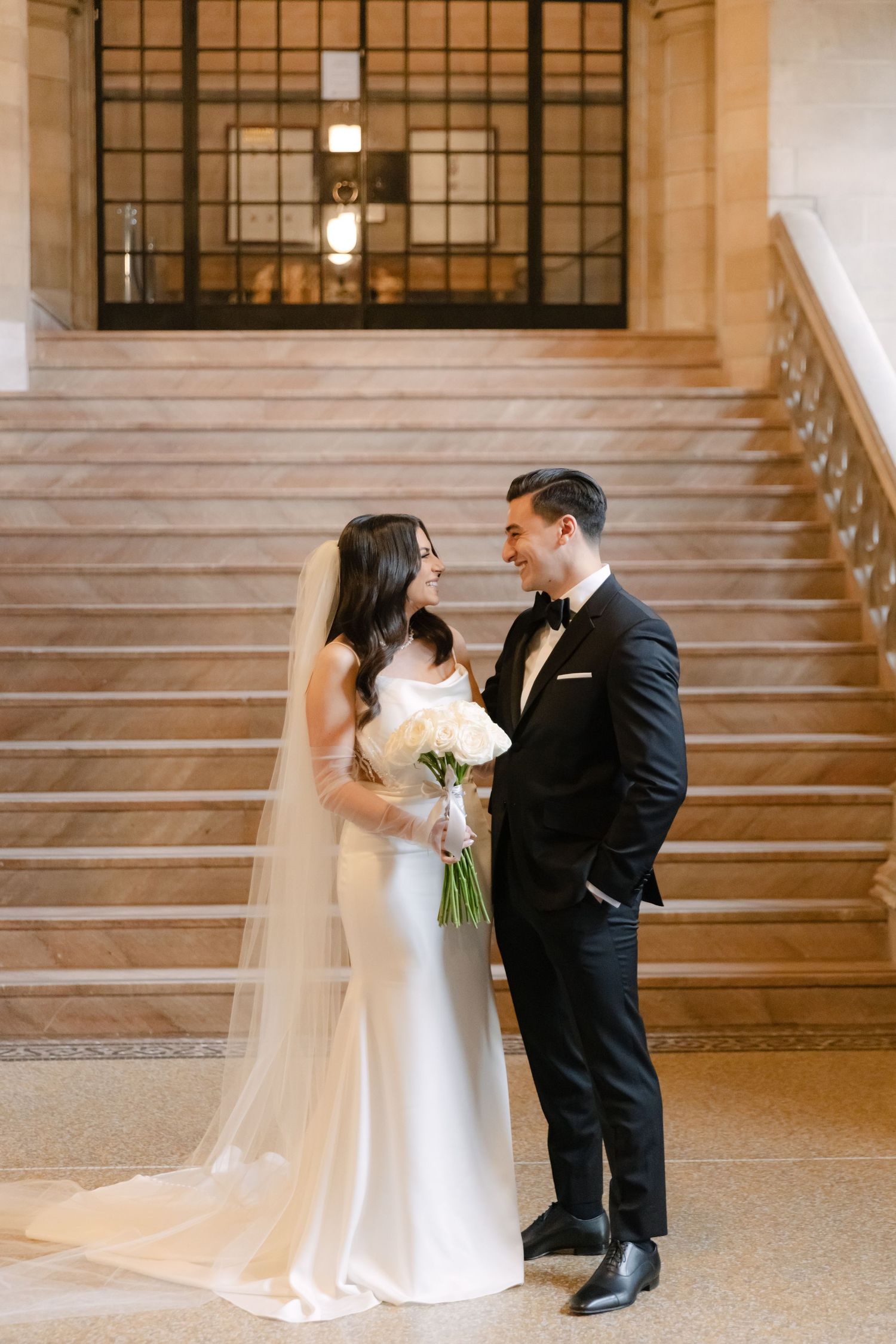 A romantic wedding portrait on classic stone steps with a white bouquet and formal attire.