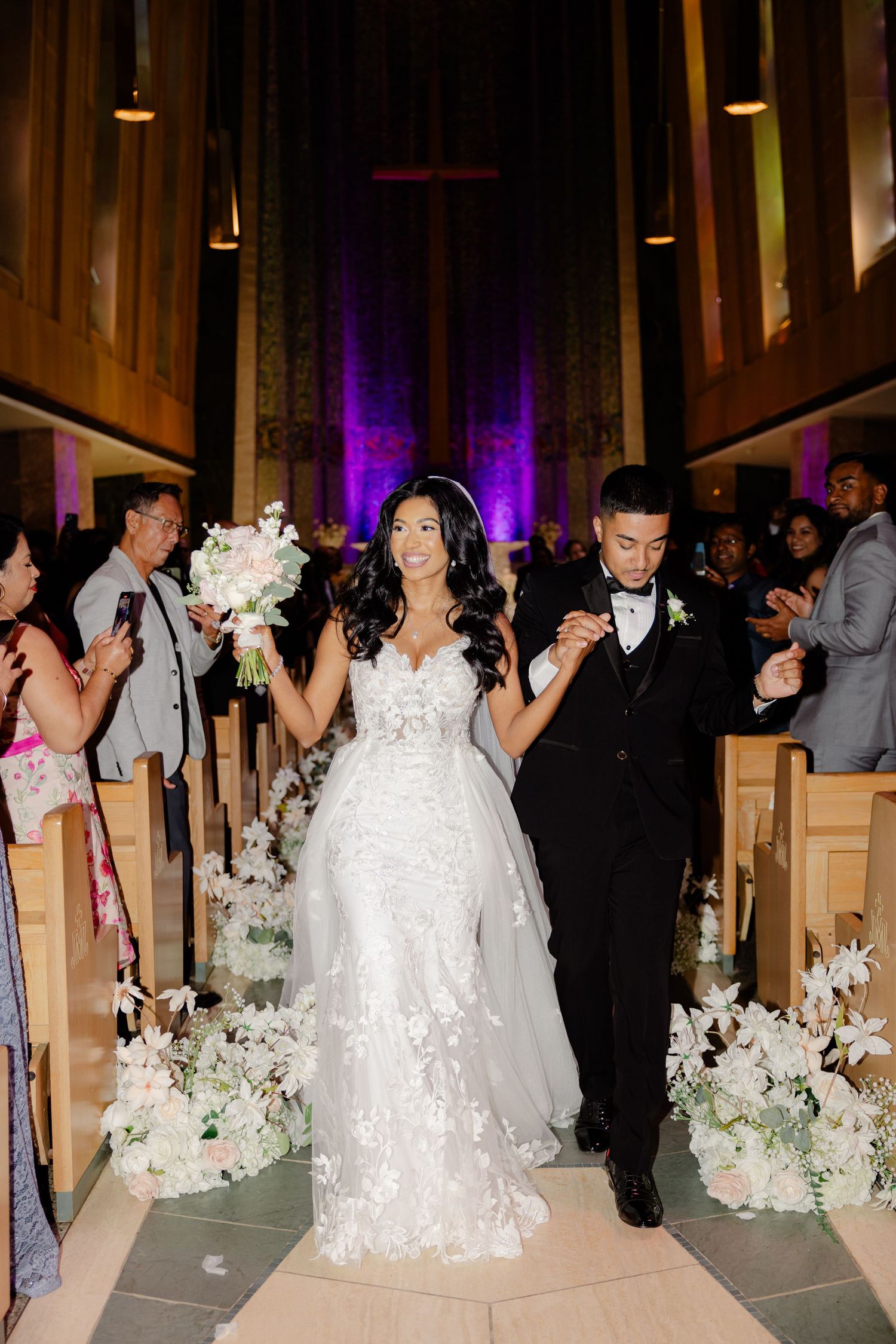 Newlyweds celebrate while walking down a flower-decorated church aisle after their ceremony.