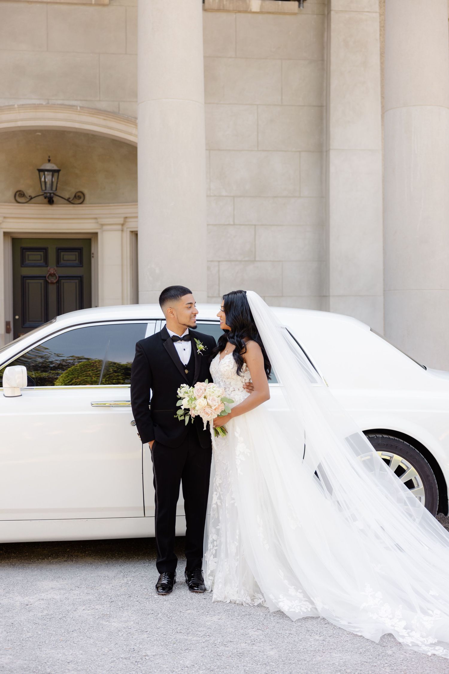 Wedding celebration with luxury white car in front of columned entrance.