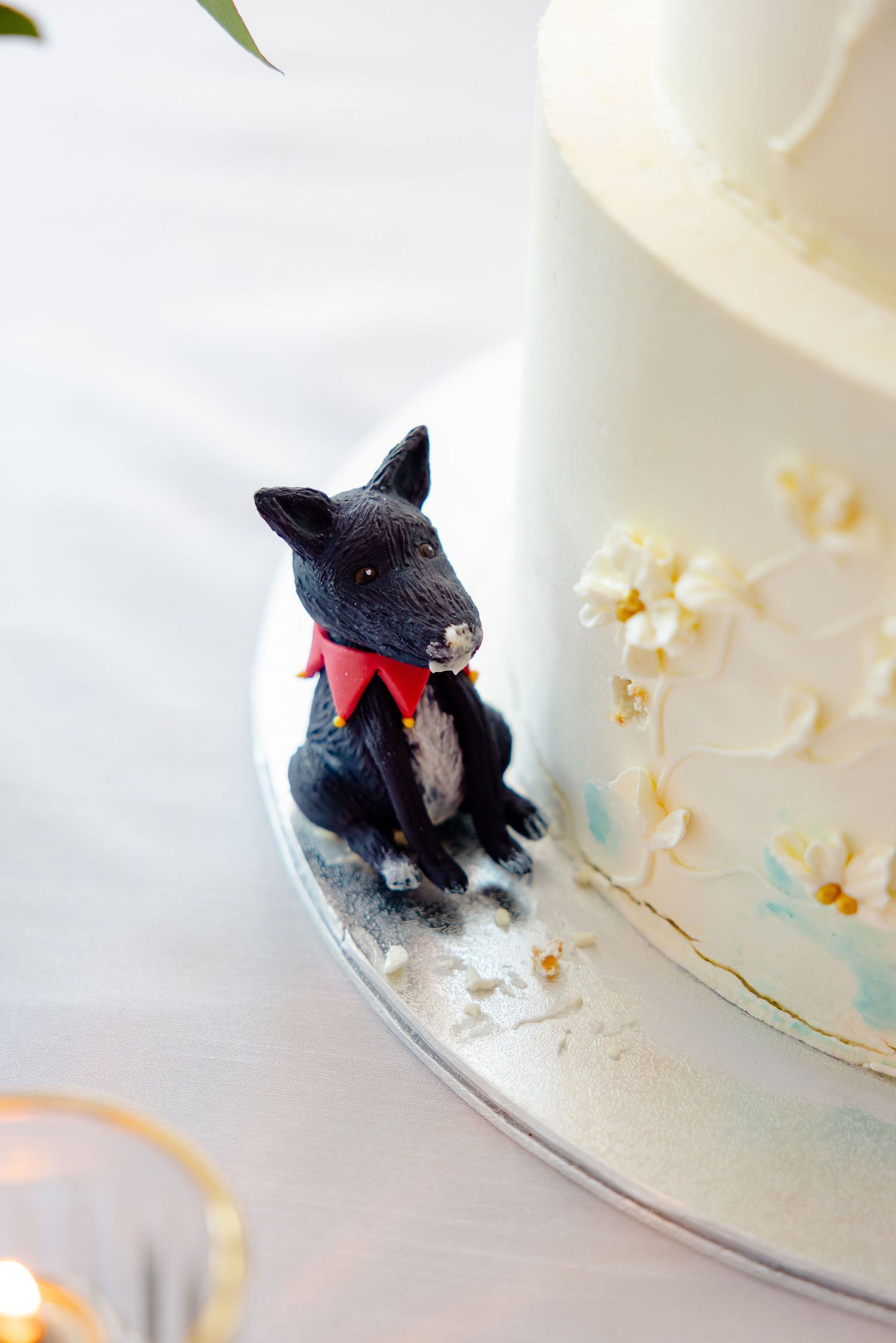 Black dog figurine with red bow tie decorating a white wedding cake.