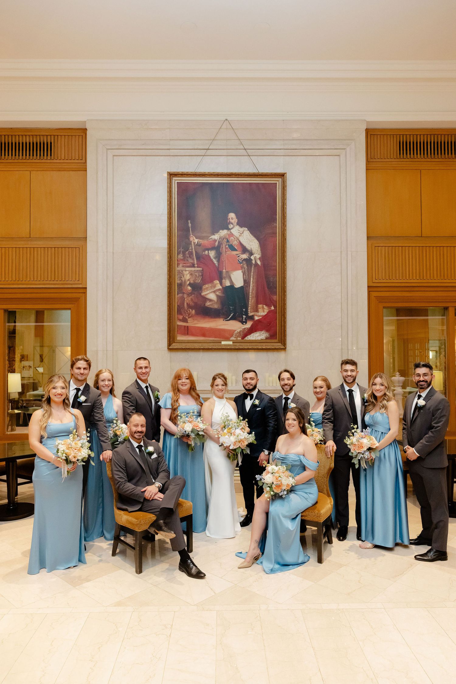 Large wedding party group photo with bridesmaids in blue dresses and groomsmen in dark suits.