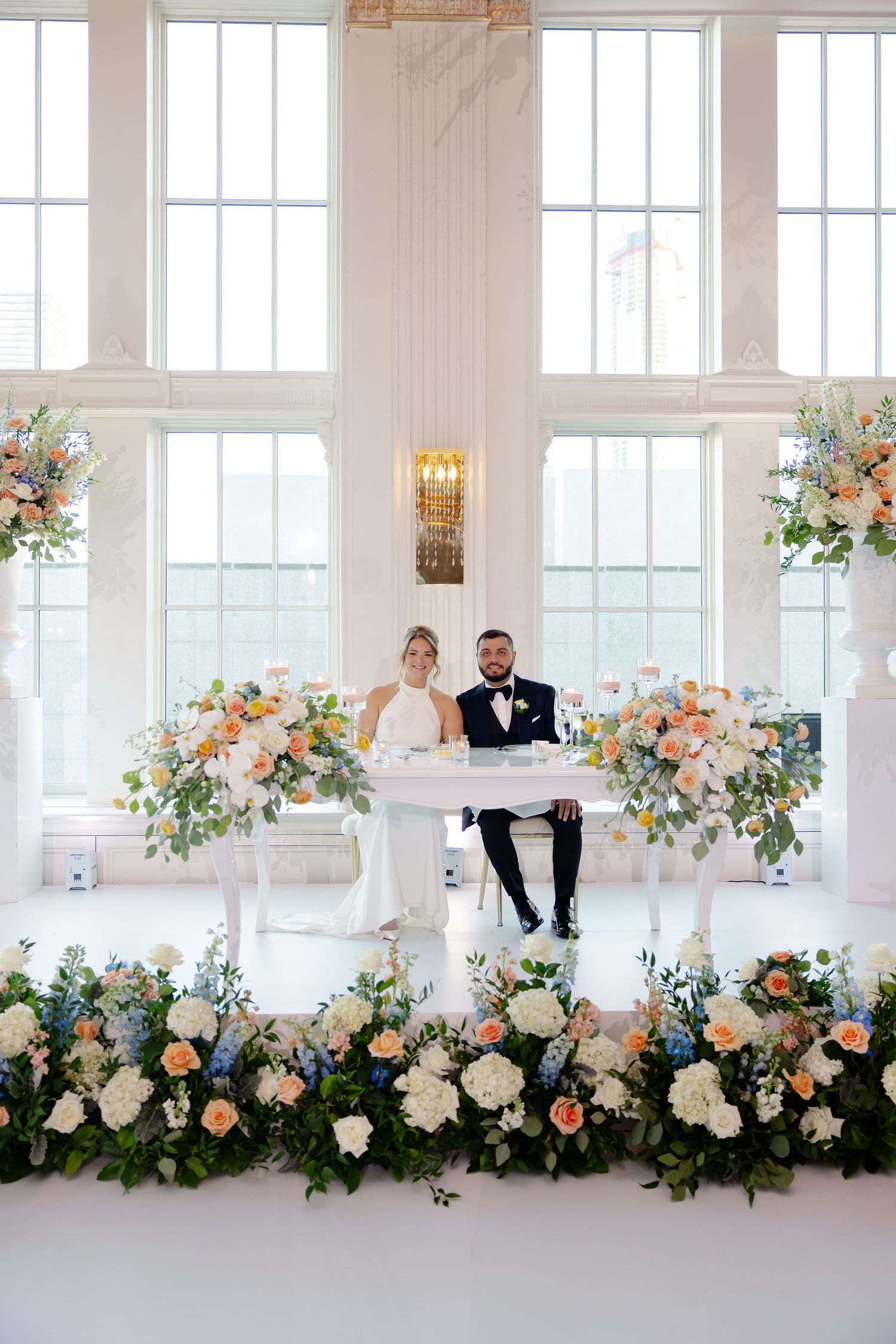 Wedding reception head table with cascading floral arrangements in peach and white.