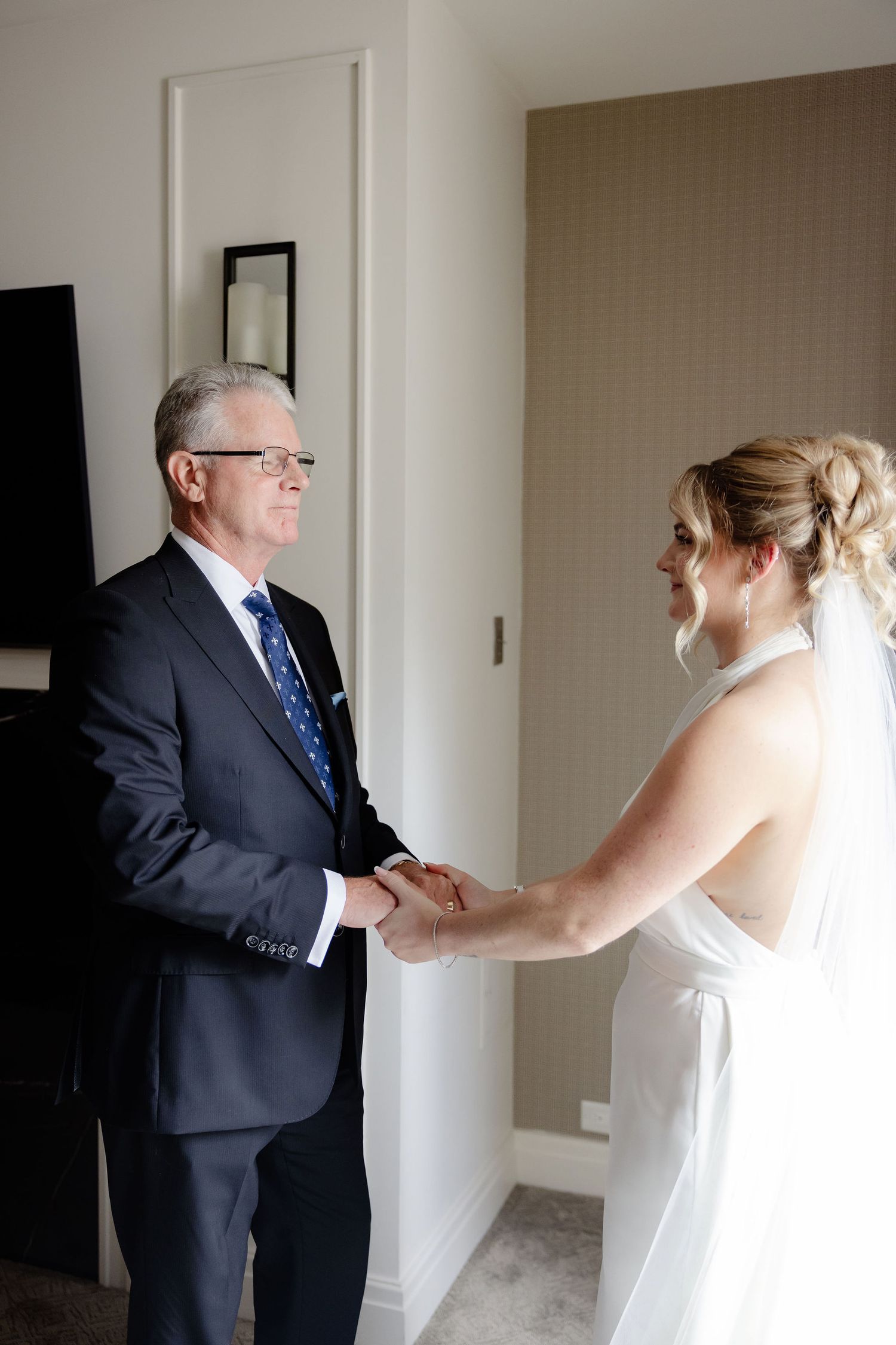 Emotional first look moment between bride and suited figure in hotel hallway.