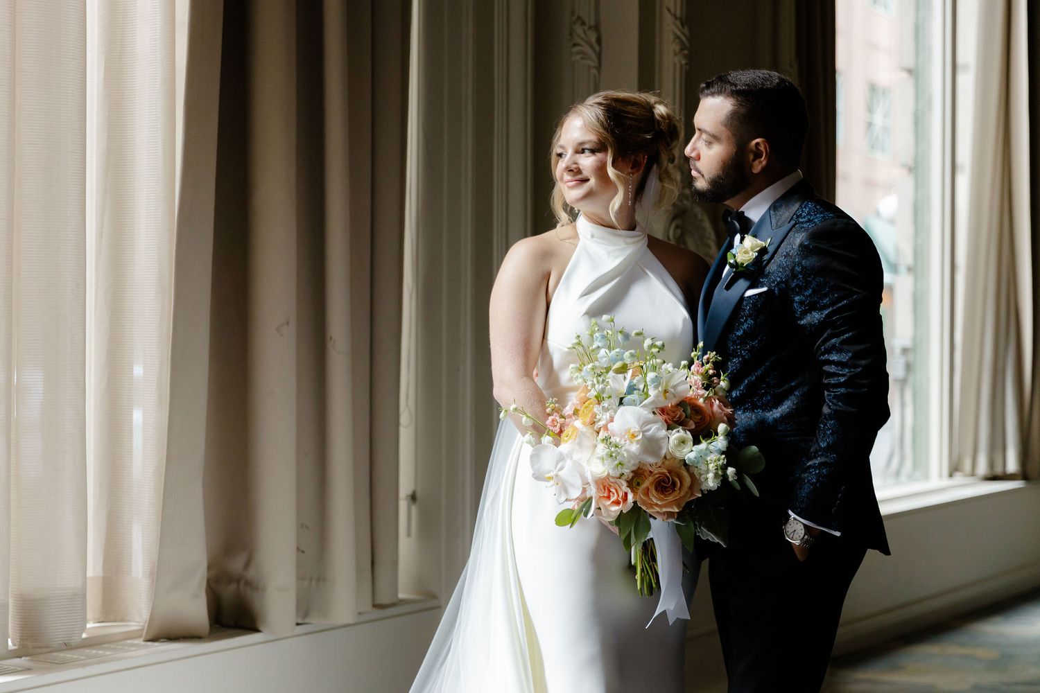 A romantic wedding first look moment captured in a grand ballroom with ornate white walls and elegant decor.