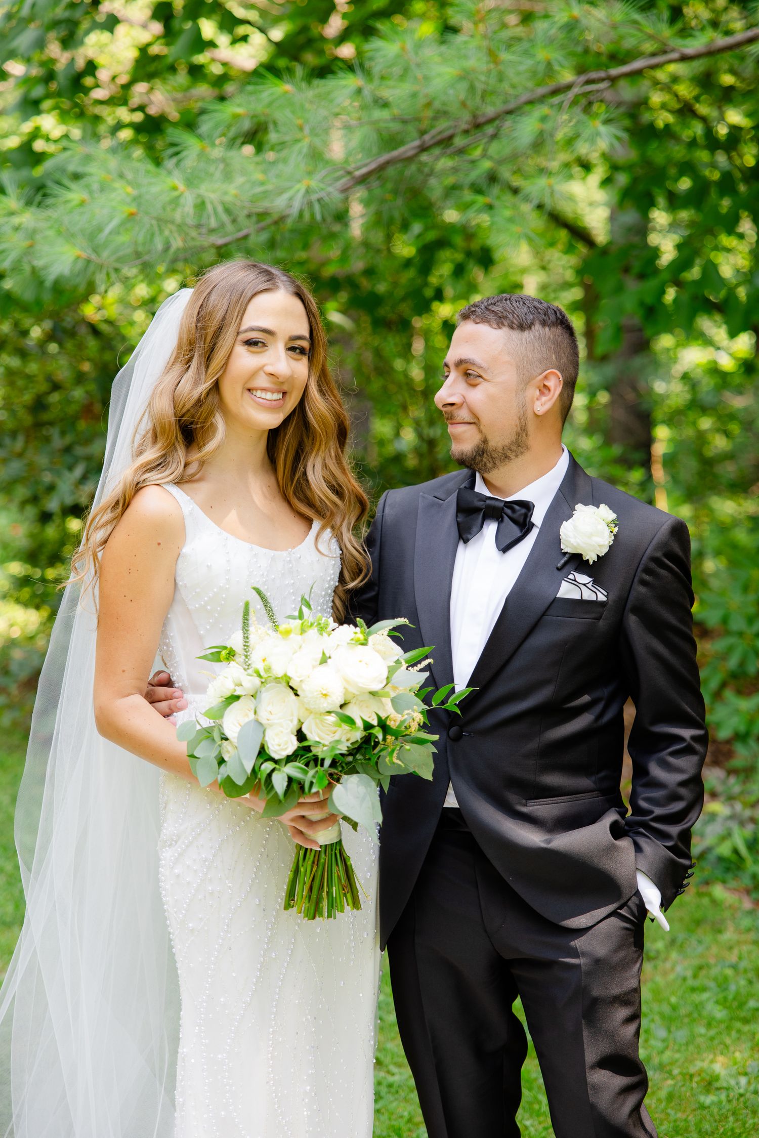 Bride in white gown and groom in black tuxedo share happy moment in garden.