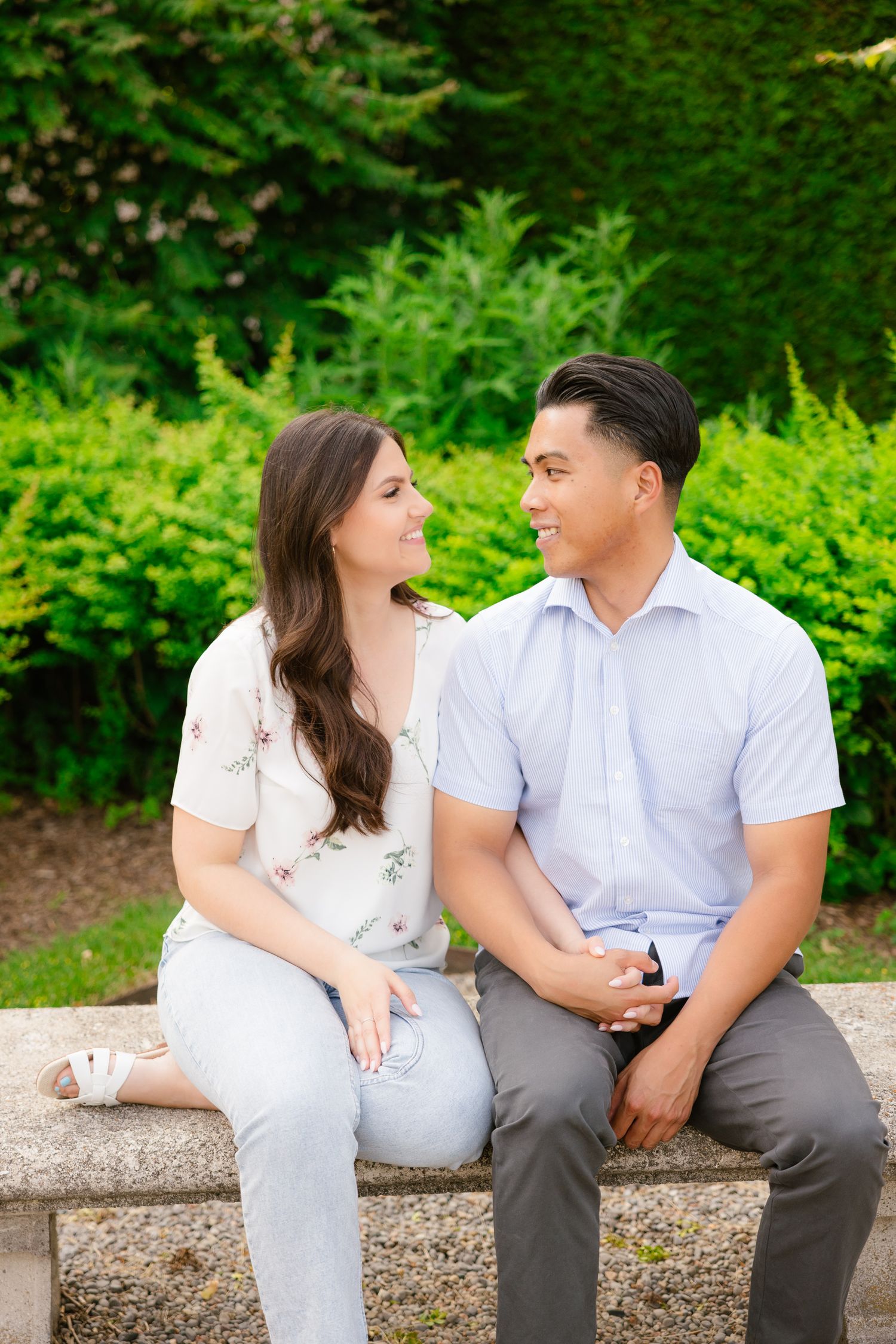 A couple in coordinating white and blue outfits share an intimate moment on a garden bench.