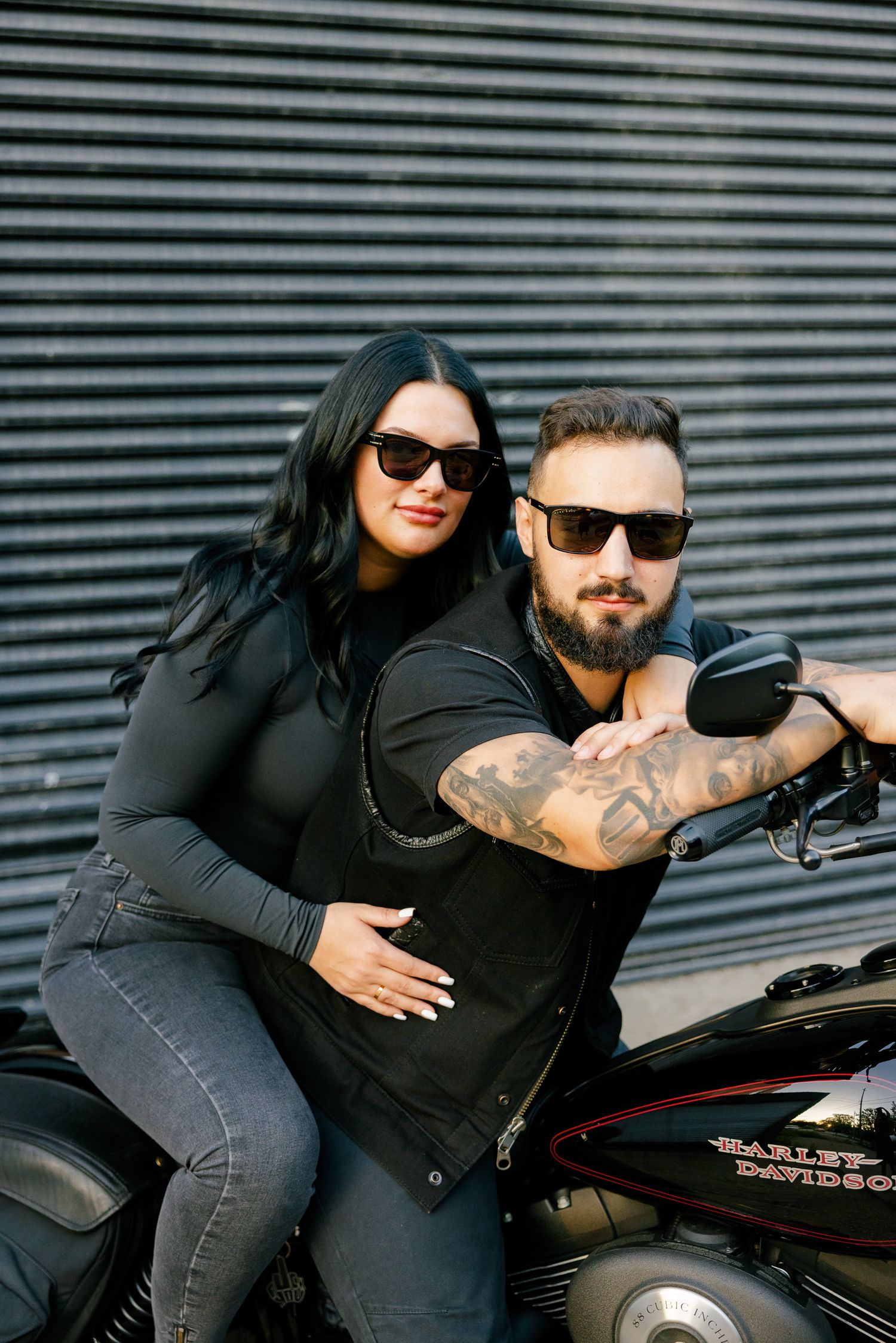 Couple on motorcycle sharing romantic moment against urban metal wall backdrop.
