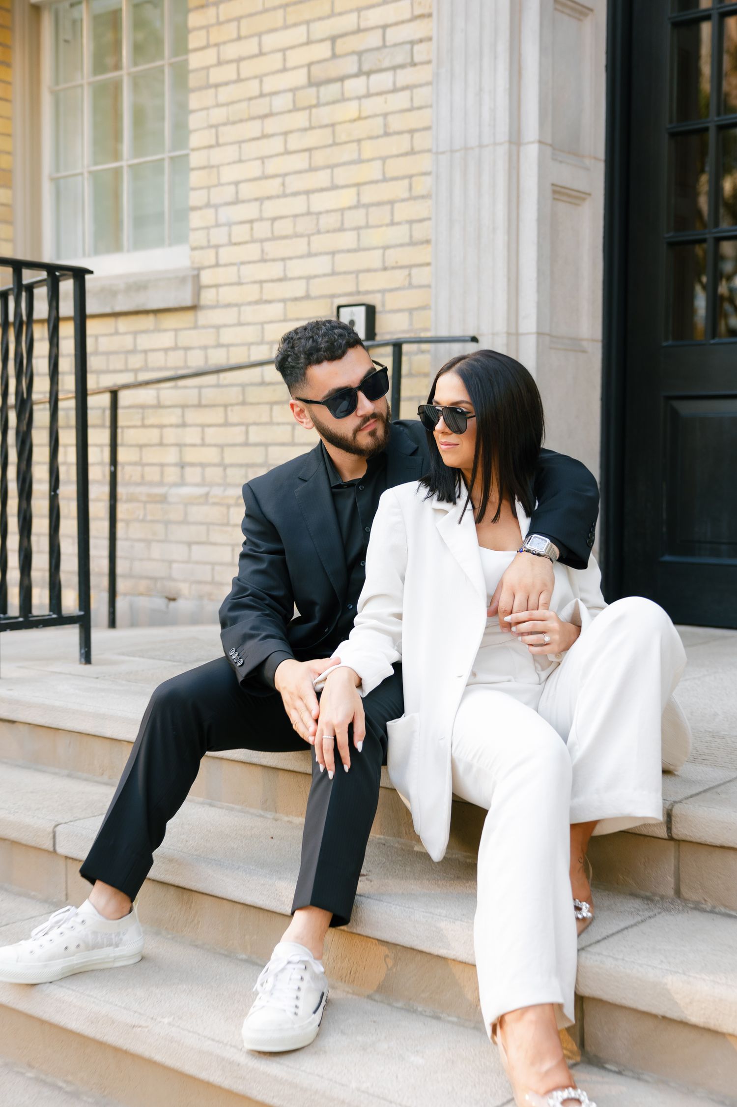 Fashionable duo in complementary outfits sitting casually on stone steps of boutique.
