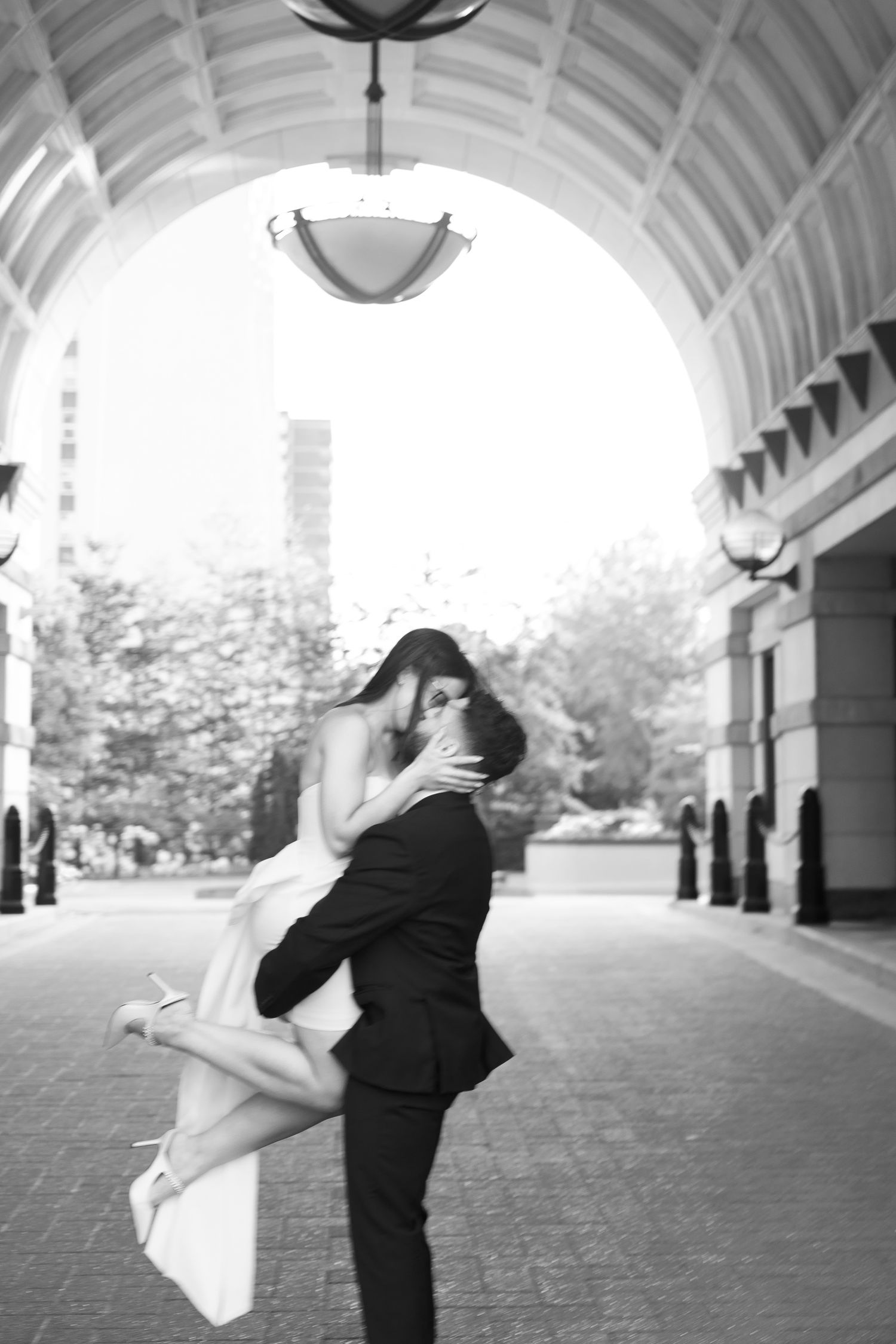 Monochrome capture of a tender moment between a couple under a grand architectural archway.