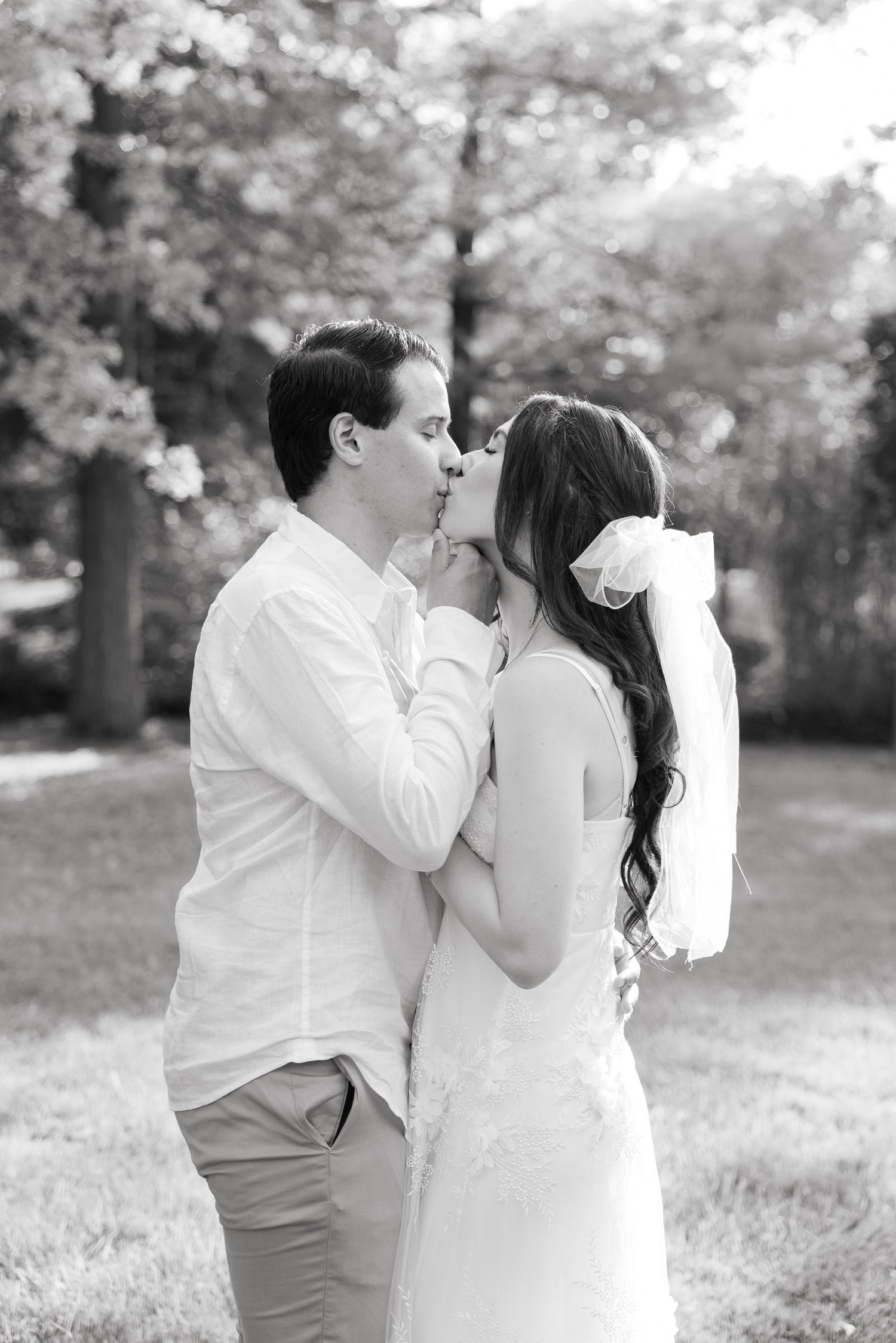 Black and white romantic portrait of a couple sharing a kiss in a garden setting.